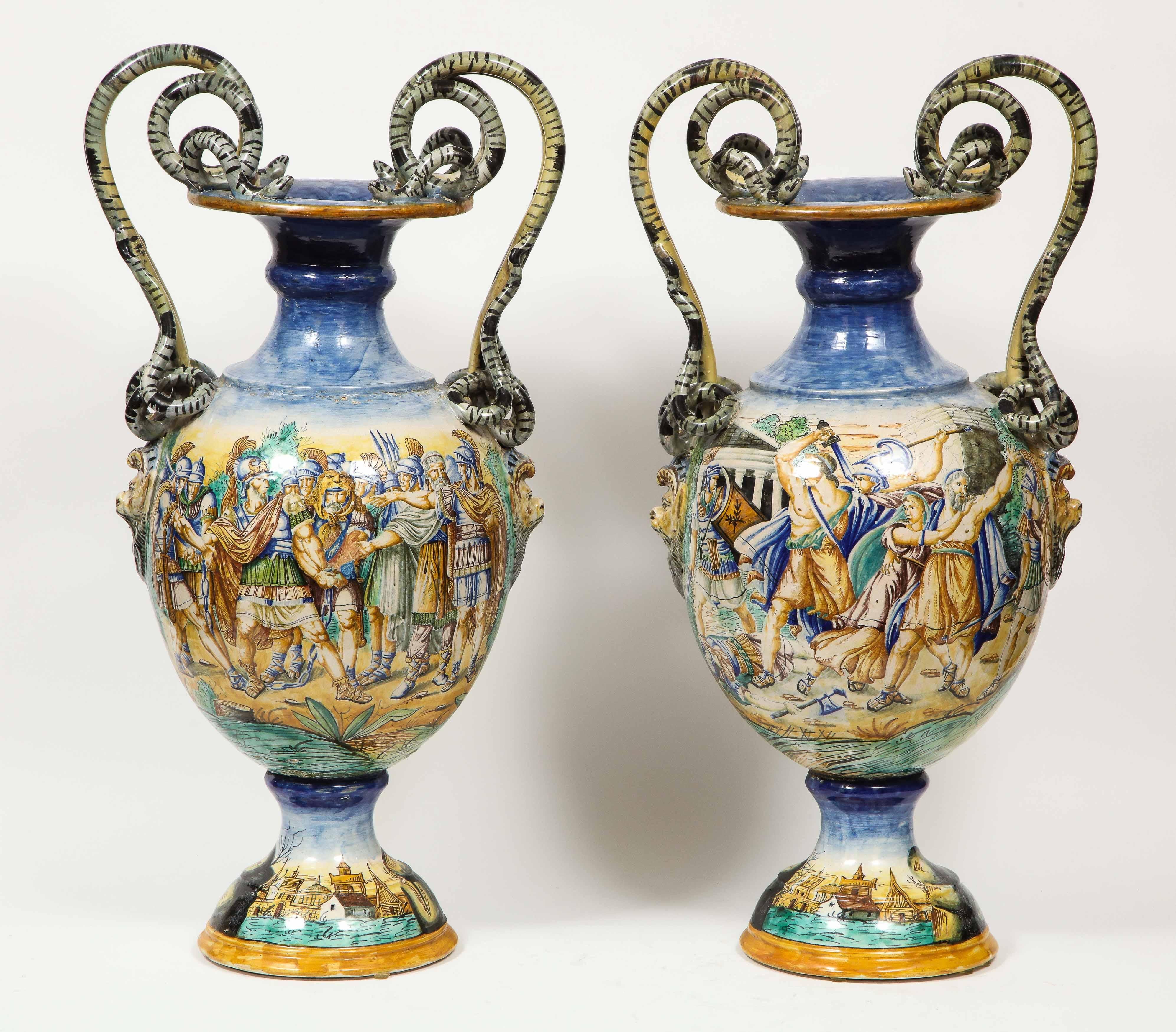 An Imposing pair of large antique Italian Majolica snake-handled vases, late 19th century.

With very fine hand painted classical and biblical scenes and grotesque faces in relief to the sides beneath each detailed snake handle.

Similar to work