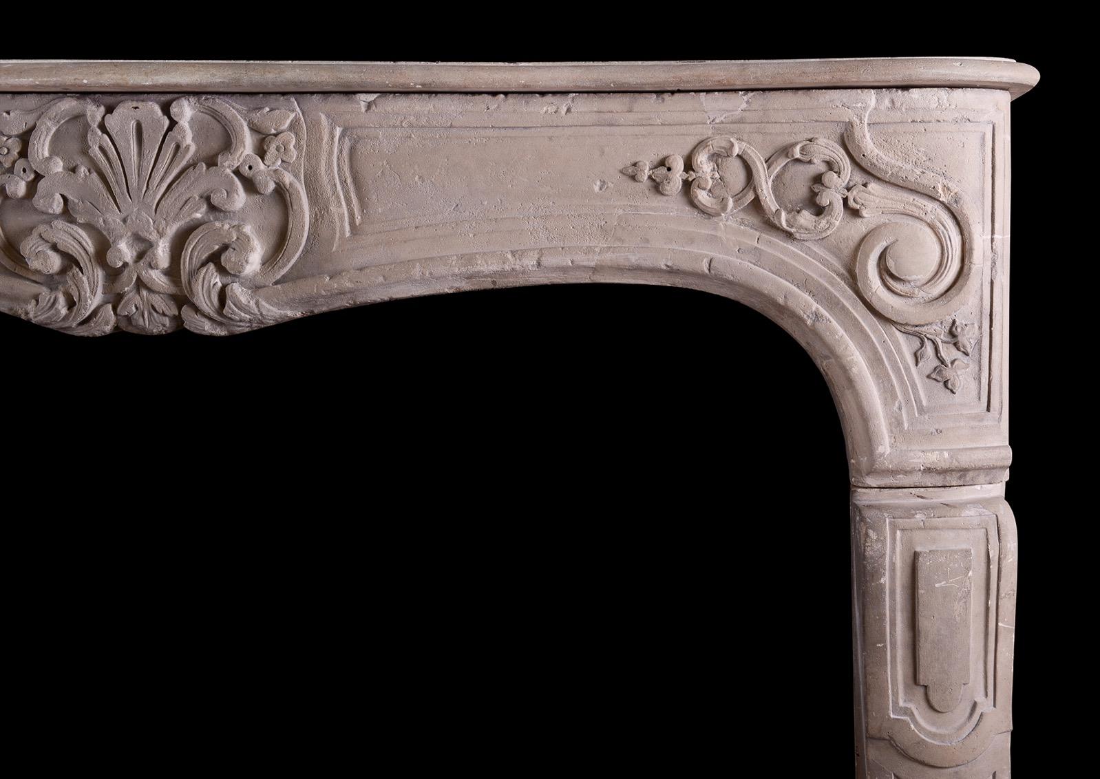 An imposing period Louis XV carved limestone fireplace. The panelling jambs surmounted by shaped frieze carved with scrolls and leaf work to centre. Shaped, moulded shelf above. Still in nicely rustic condition, but could be restored further if