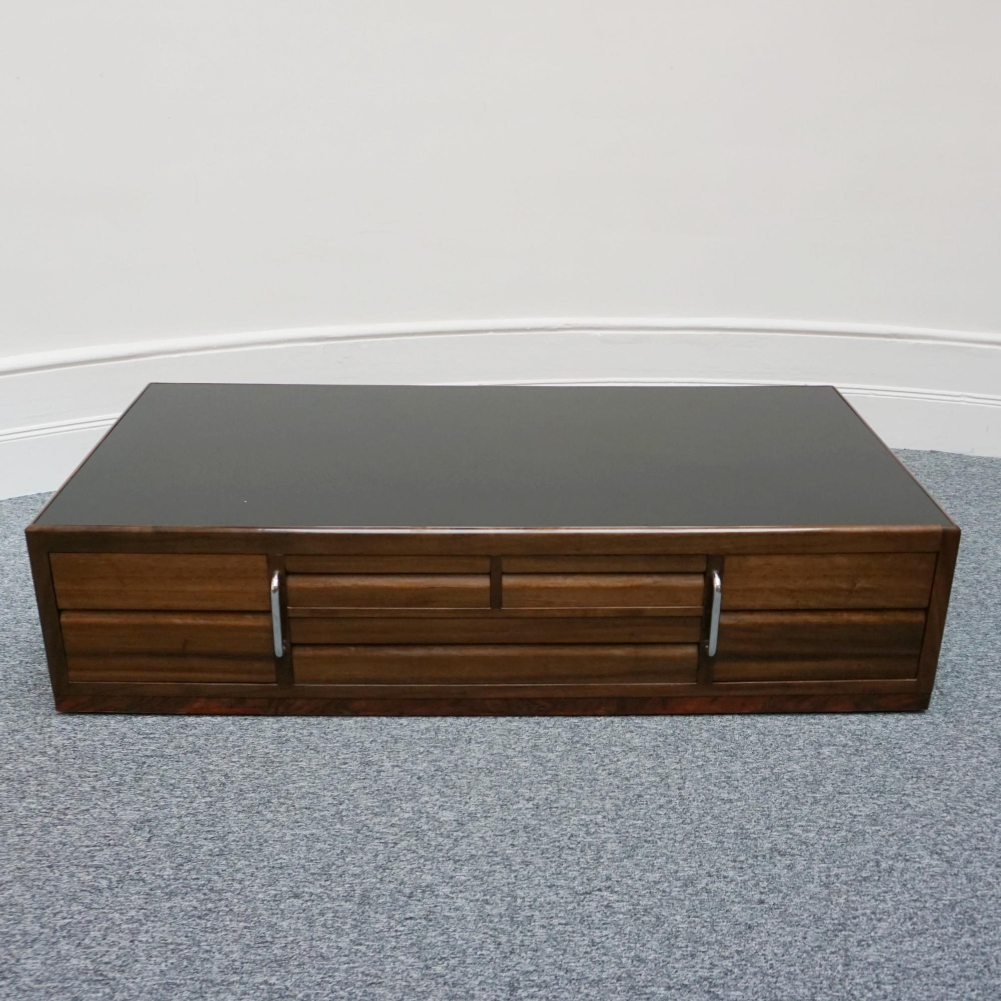 An Art Deco coffee table by Betty Joel. Australian walnut veneered with burr walnut banding. Extensive integral storage with two chrome handles for moving. Set over original castors. Original black glass top. Signed and dated to back. 

Dimensions: