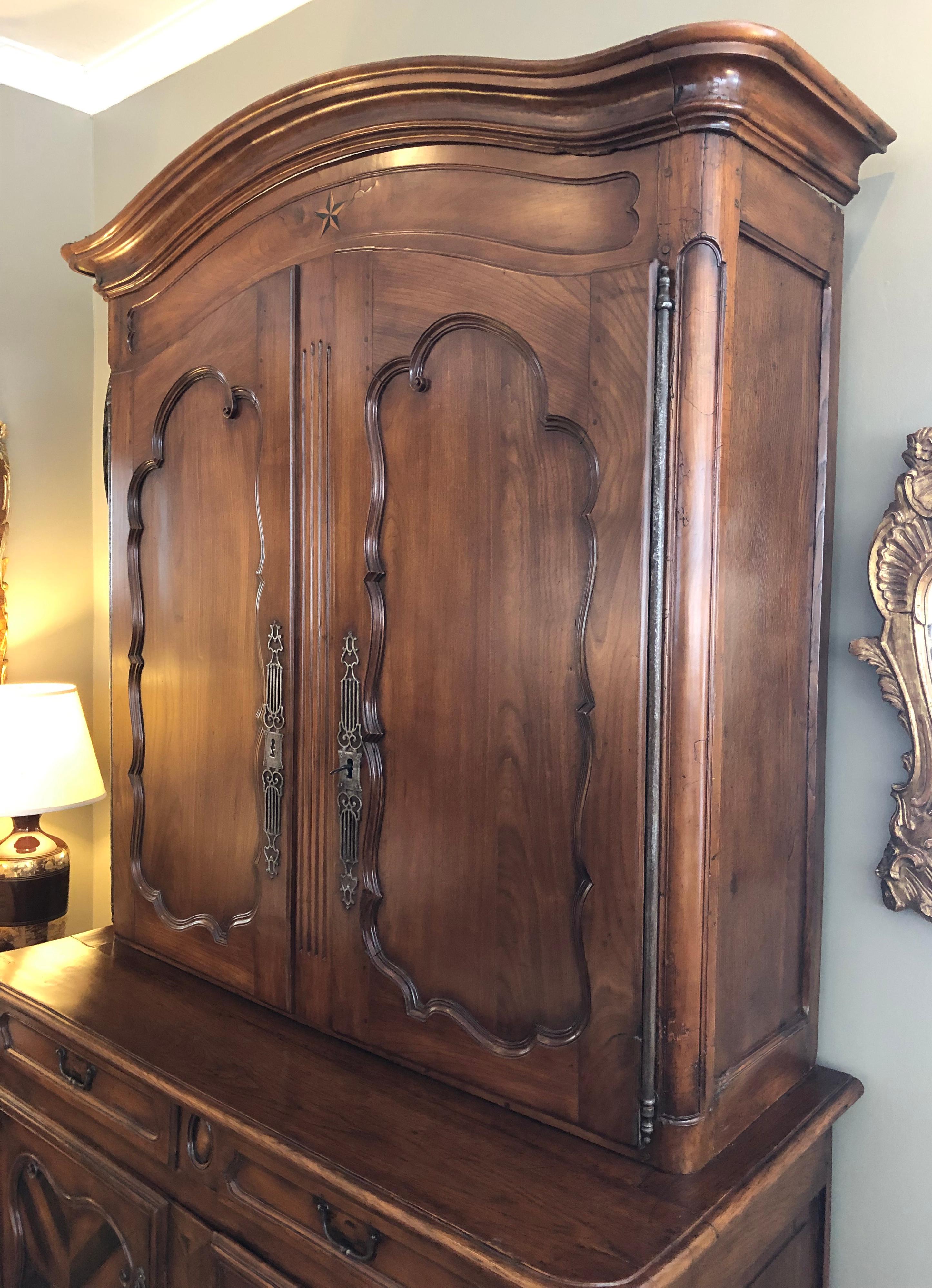 In two pieces, the dramatic arching crest above a two-door cabinet resting on a base fitted with two short drawers over 2 doors.