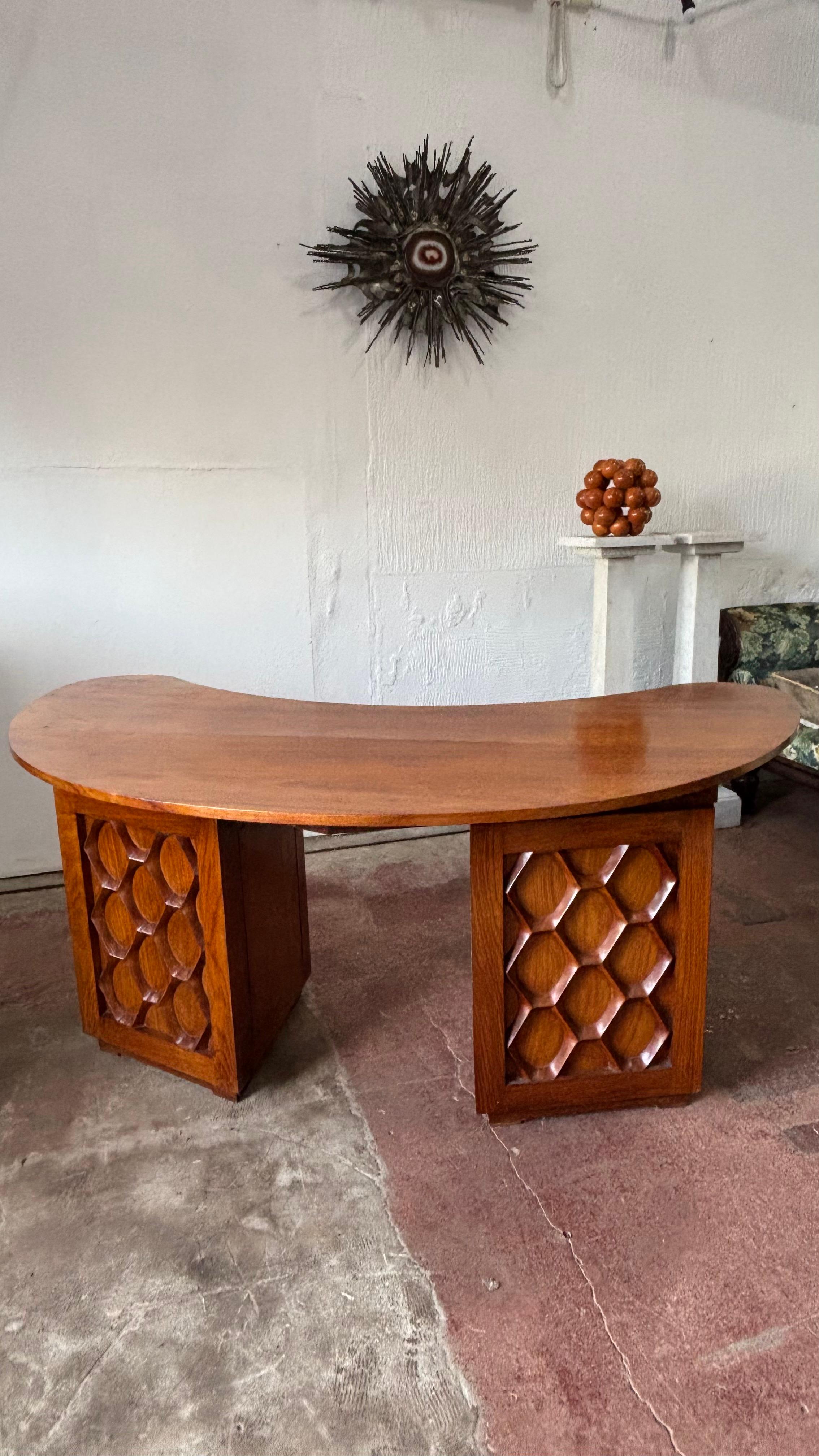 A teak desk of boomerang form, large and stately size. The twin pedestal featuring beautiful brass handles that are in the form of Sanskrit Seal. These feature animals. The drawers open on the angle and the bottom drawer pulls out and is fitted for