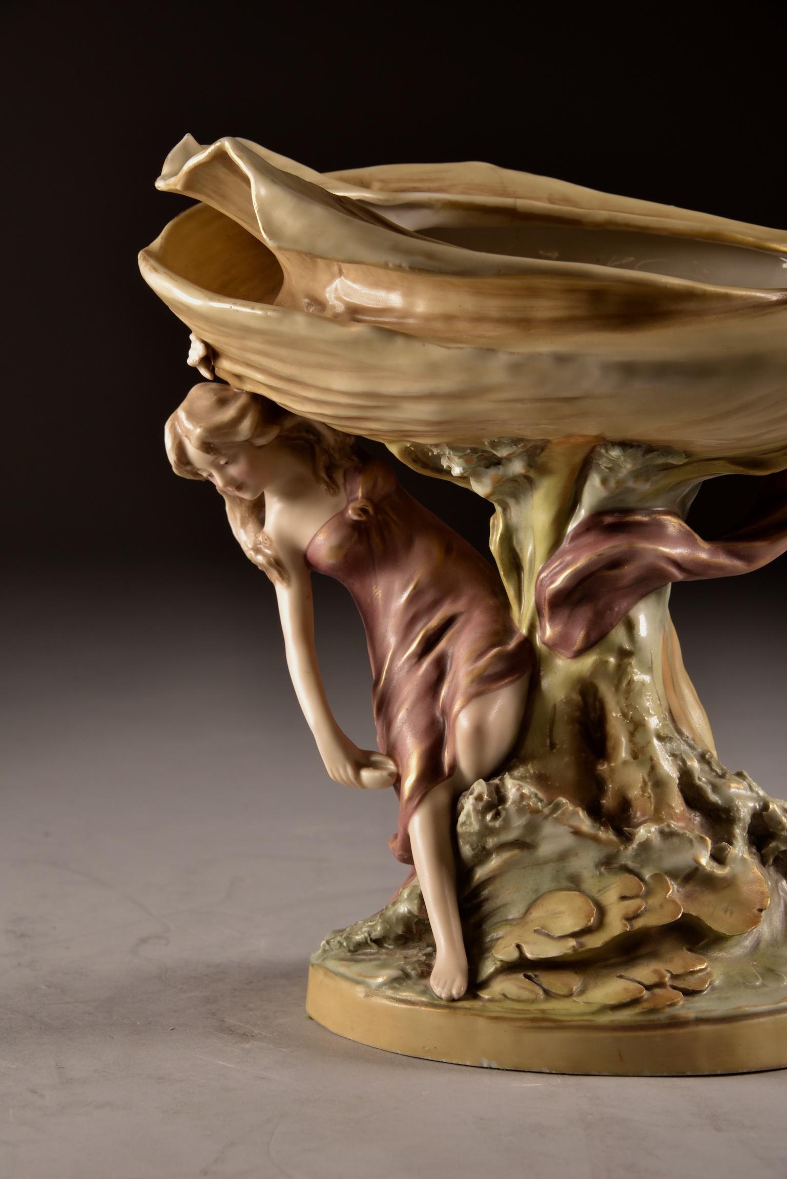 Splendida porcellana Royal Dux Bohemia, design Art Nouveau con due fanciulle appollaiate su una grande conchiglia montata su un piedistallo. La fabbrica Royal Dux divenne famosa per le sue figure umane, animali e fiori dai colori terrosi. Questo