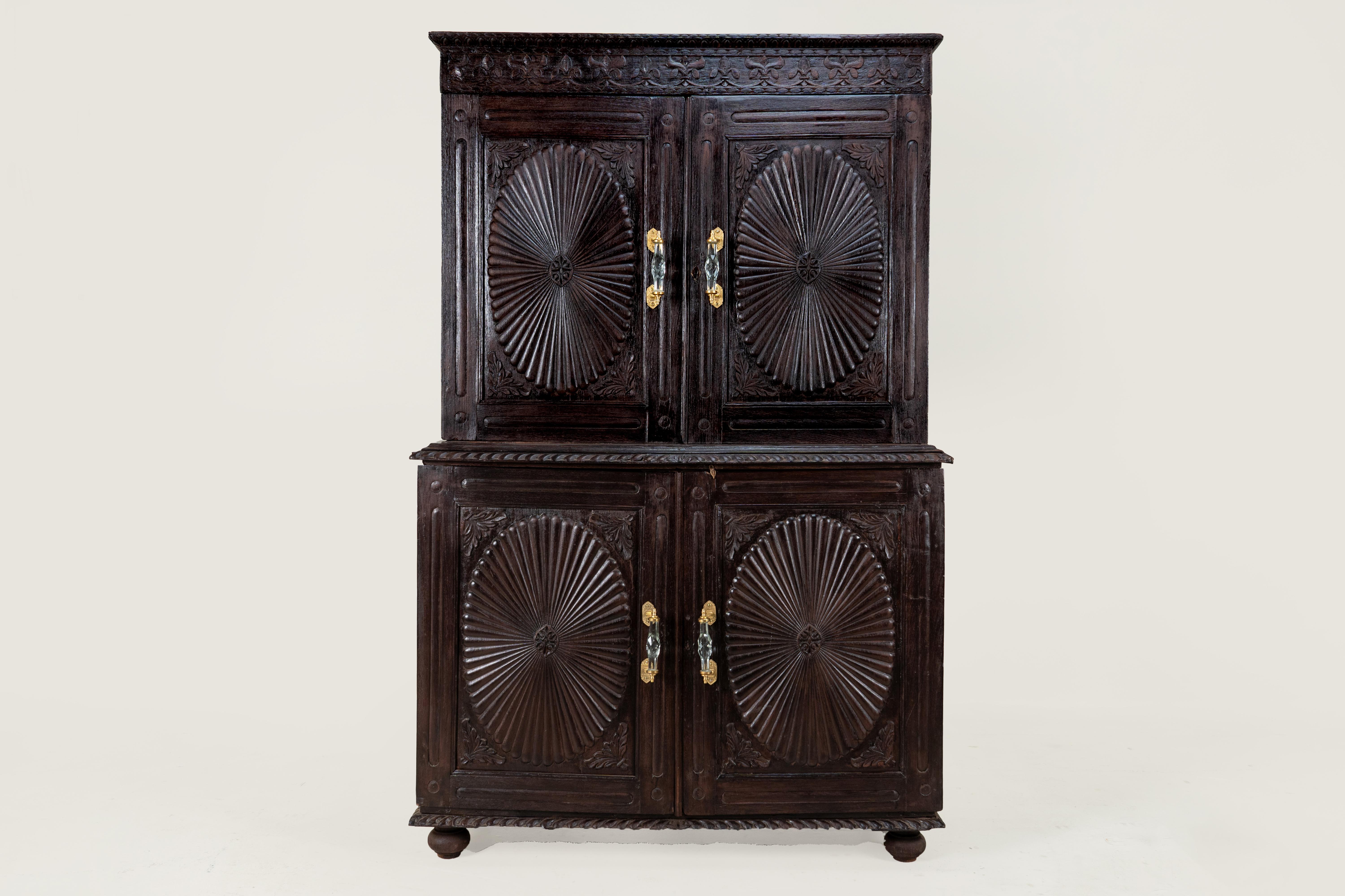 Un bell'armadio indiano Art Deco di Ahmedabad, 1930 circa, scolpito in teak massiccio. Gli audaci medaglioni a raggiera che si irradiano su ogni porta creano un senso di movimento e di luce, caratteristiche del fascino Deco per la geometria e