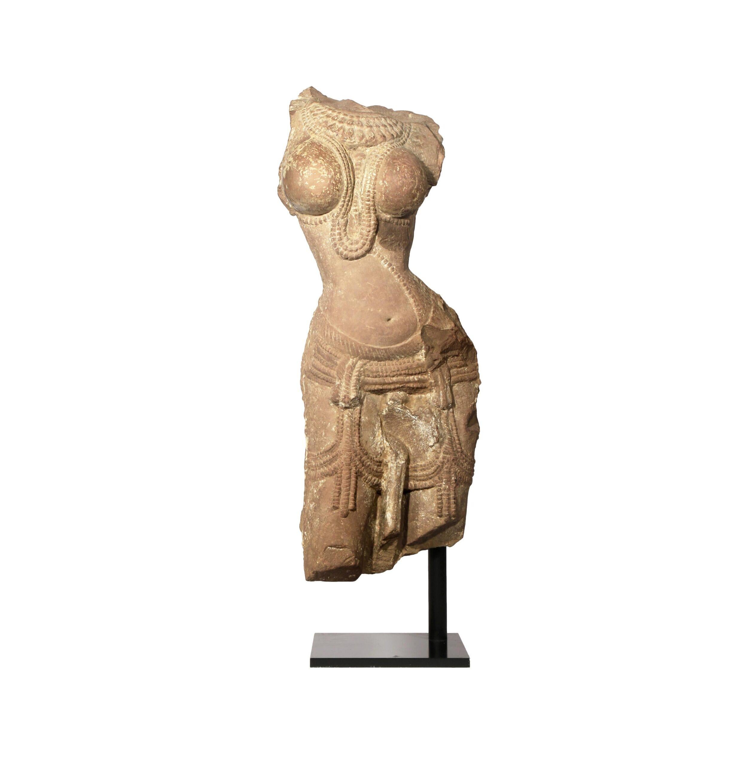 An Indian Red Sandstone Torso of a Devata, Probably Rajasthan, the female deity depicted in tribhanga, her voluptuous body adorned with elaborate jewellery, wearing a sheer dhoti secured with a belt, all supported on a modern stand, 69cm