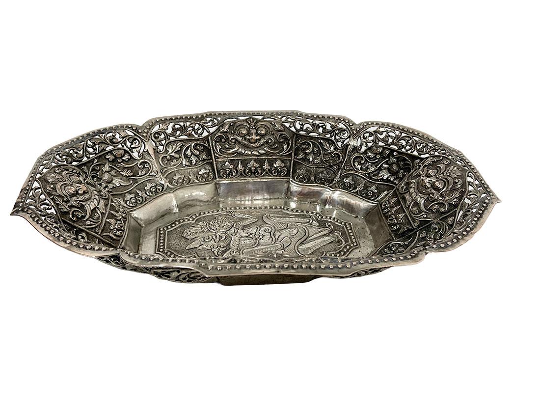 An Indonesian Yogya basket, ca 1900

An Indonesian, Bali, low silver content (800/1000) large basket. A large basket with scalloped edges. The top edge is openwork with floral motif. Each side in the middle a Kalakop (a mask of a monster lion)