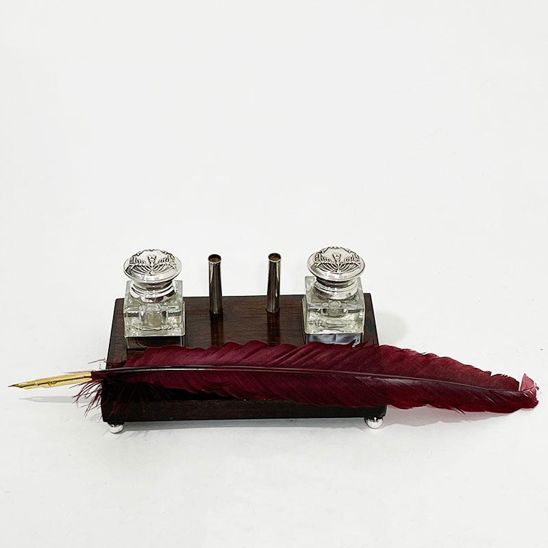 An ink set with feather pen

An inkstand on a rectangular wooden base raises on 4 ball feet with 2 holders for the ink bottles. The inkwells are made of glass with hinged lids. Marked with control marks of 925 silver. (scale 925/ eagle 925)
A