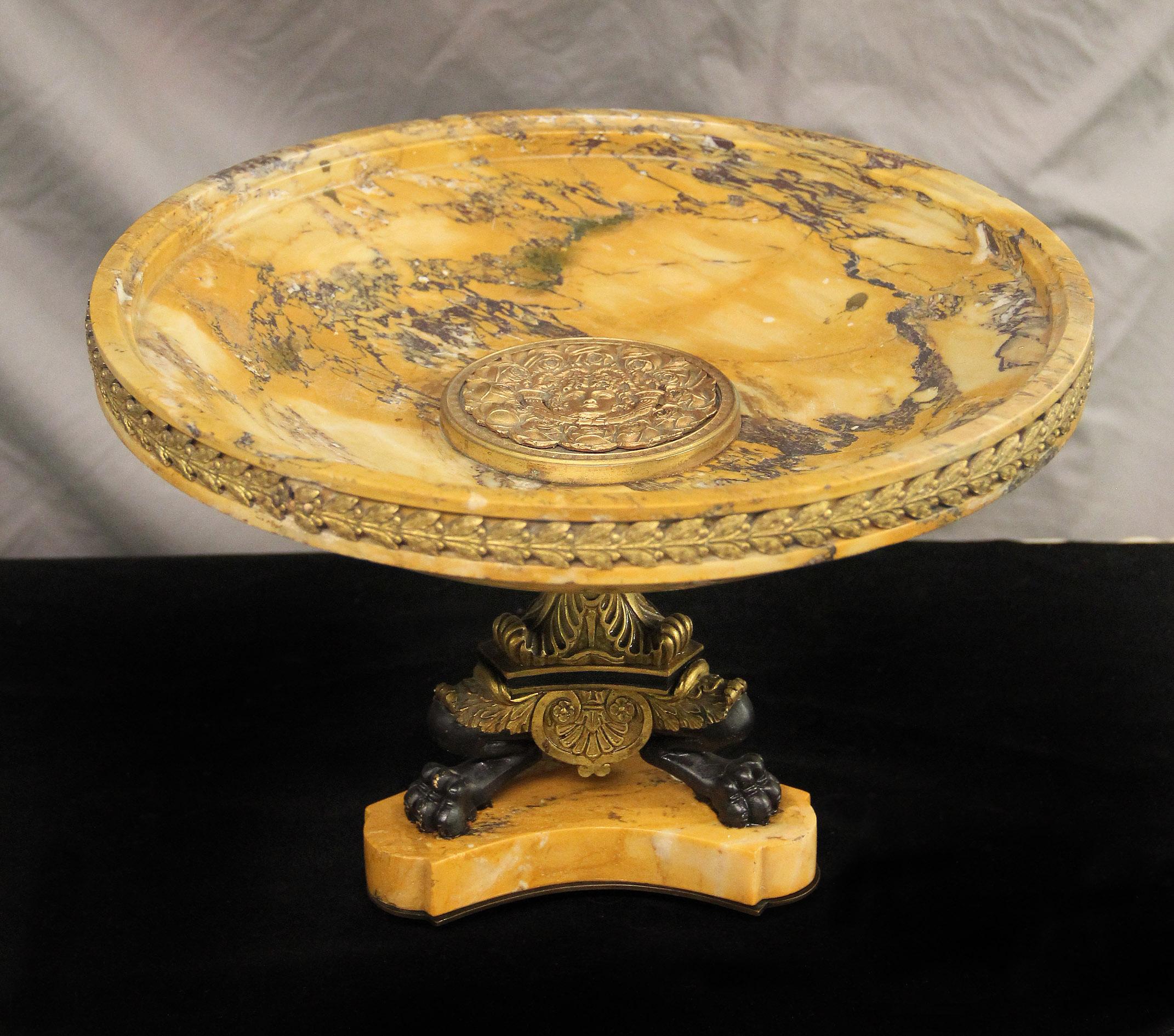 An interesting late 19th century bronze and marble centerpiece

A large marble plate centered with a bronze medallion of Apollo surrounded by roses, the base with gilt and patina bronze paws.