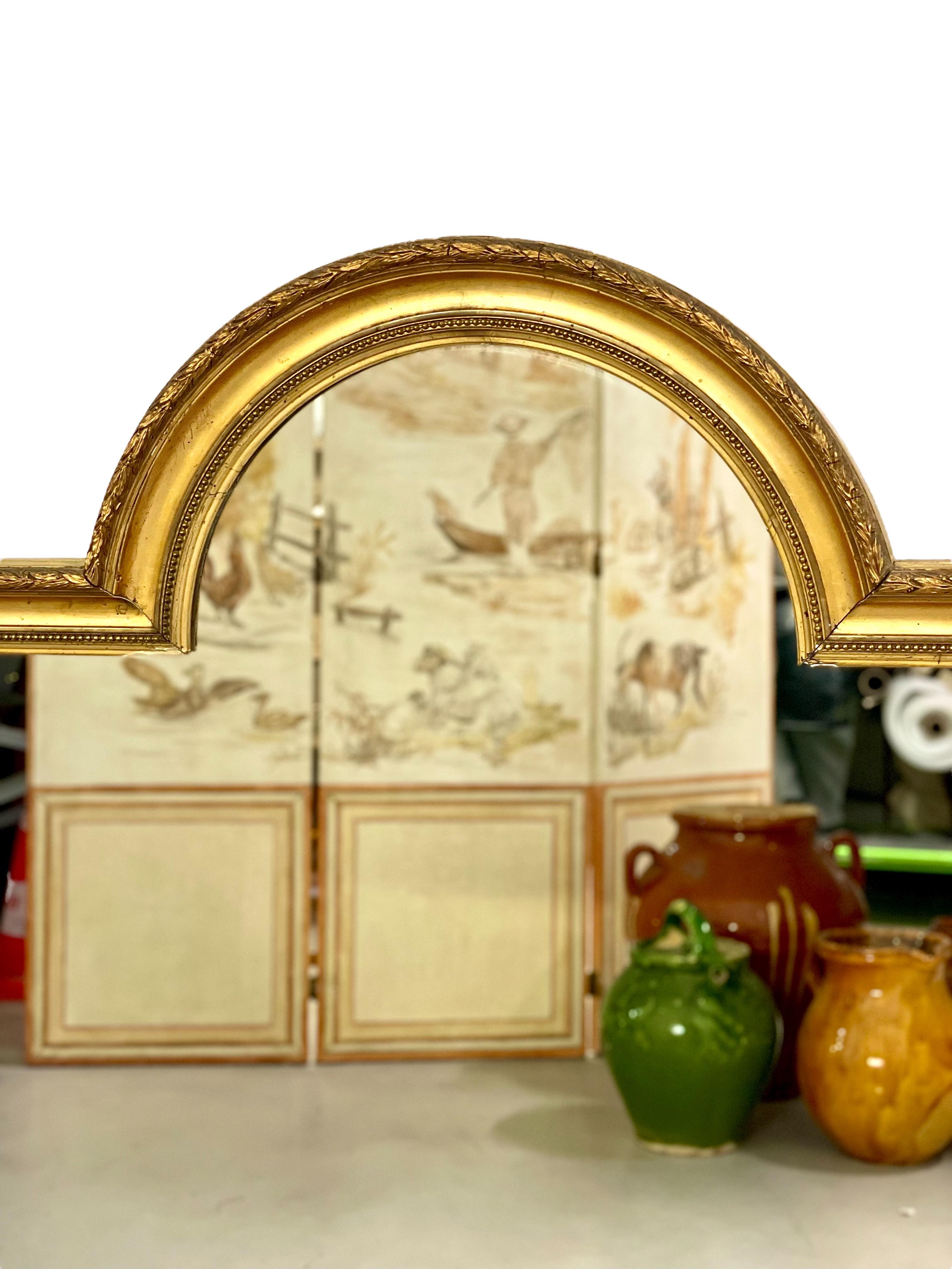 An interesting and unusual-shaped Louis XVI style overmantel mirror with central arch, in gilded wood and stucco. The outer frame features a simple chain of olive leaves, while the inner border is adorned with classic string-of-pearl beading. The