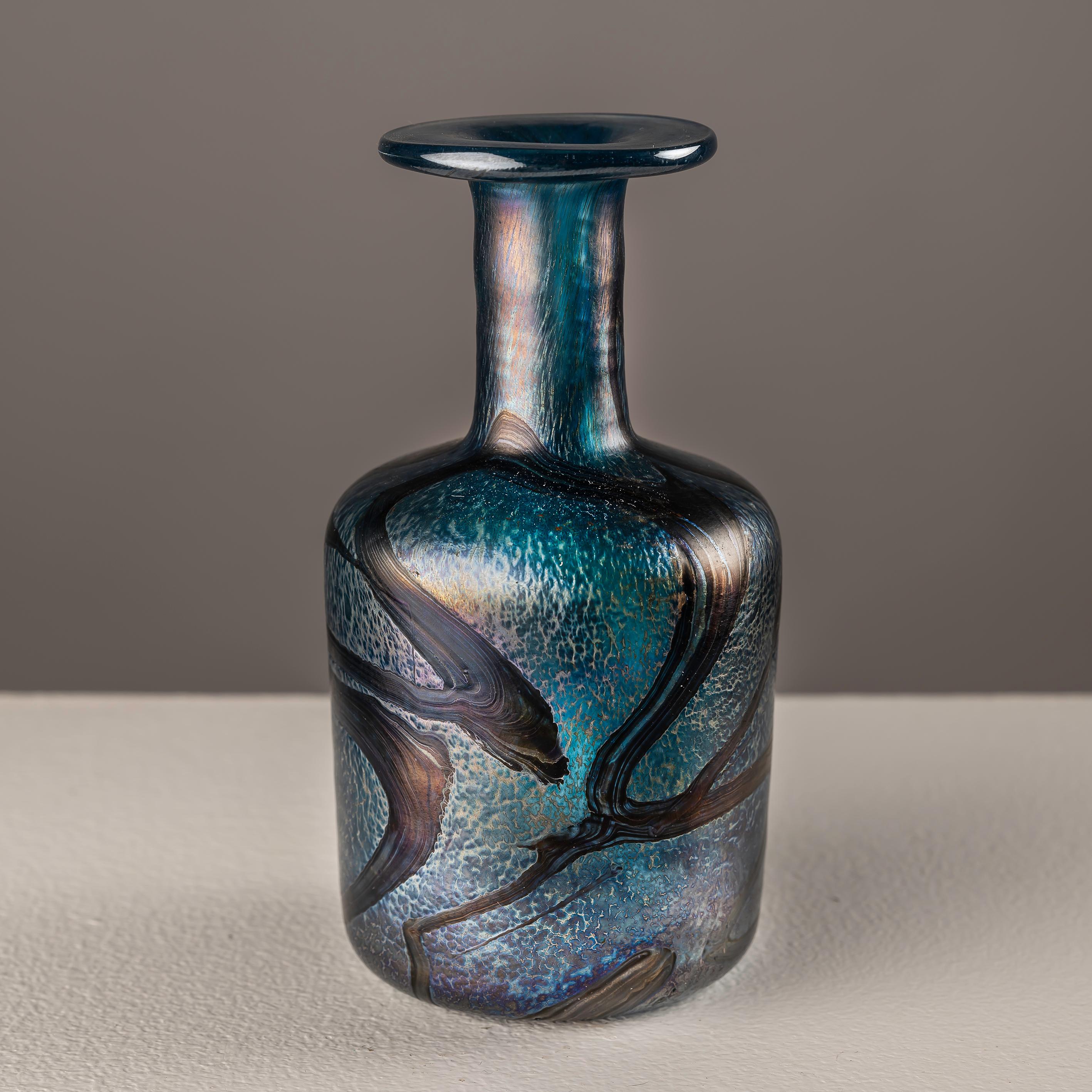 This iridescent glass vase, bearing a signature, holds a unique charm and significance. Its beauty lies not only in its mesmerizing iridescence, which reflects a spectrum of colors in the light, but also in the presence of the signature. The