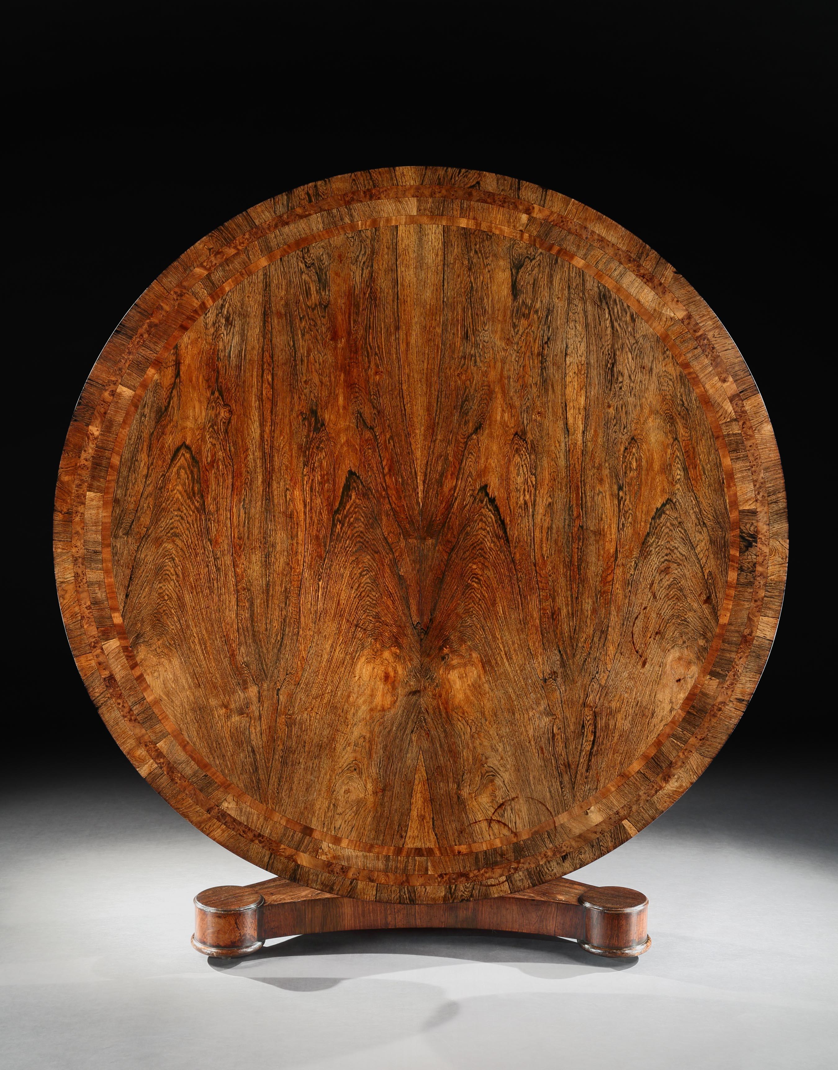 A large Irish Regency Rosewood centre table, the well figured top inlaid with a yew wood band, which is repeated on the frieze, above a turned central column carved with acanthus, resting on a plate-form base, with large bun feet and concealed brass