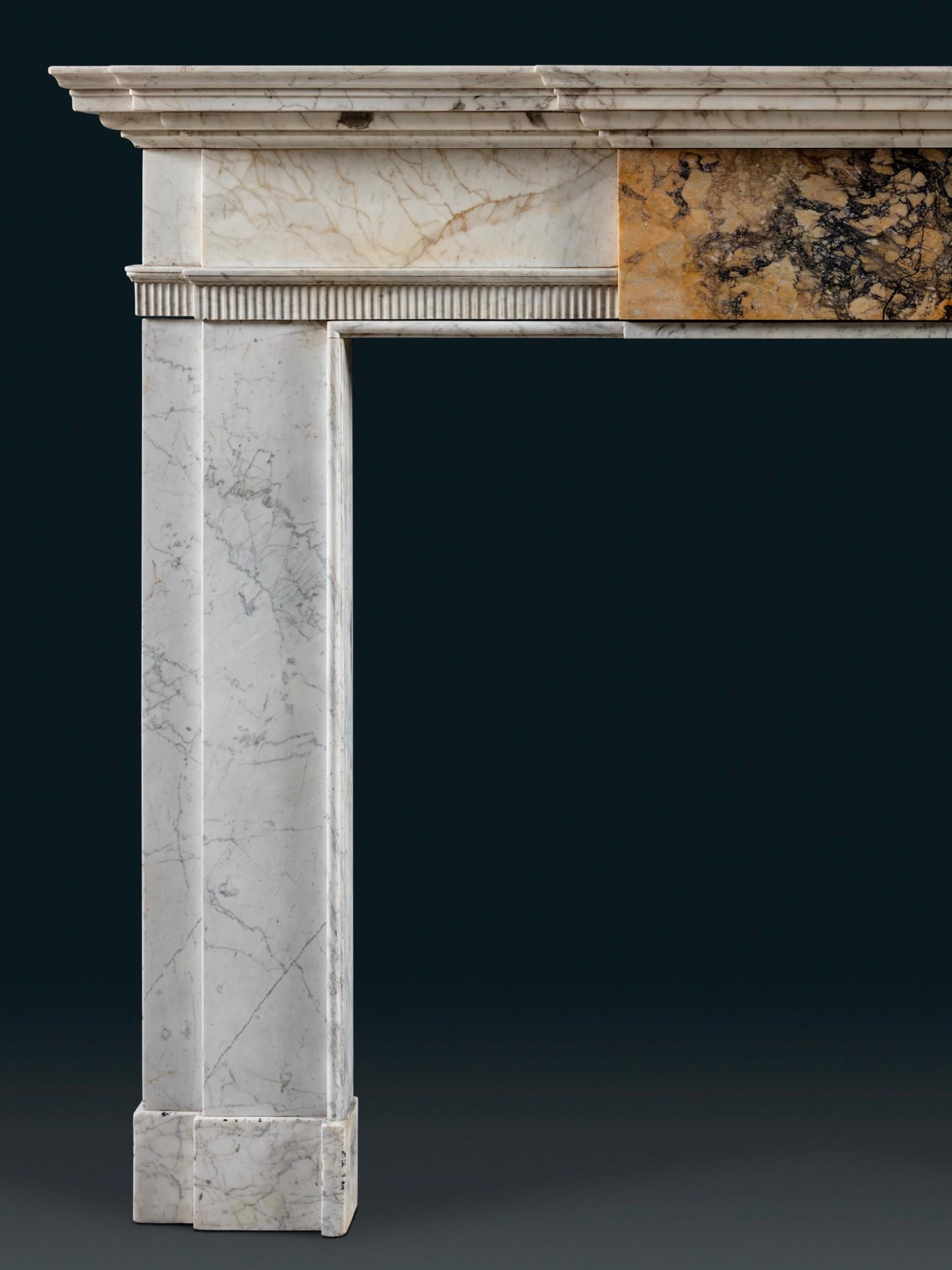 Chimenea de finales del siglo XVIII tallada en Carrara inglesa antigua con finas vetas de lápiz de forma arquitectónica sobria. La repisa del frente preside una llamativa tabla, un ejemplar de mármol Convent Sienna interrumpe el opulento uso de