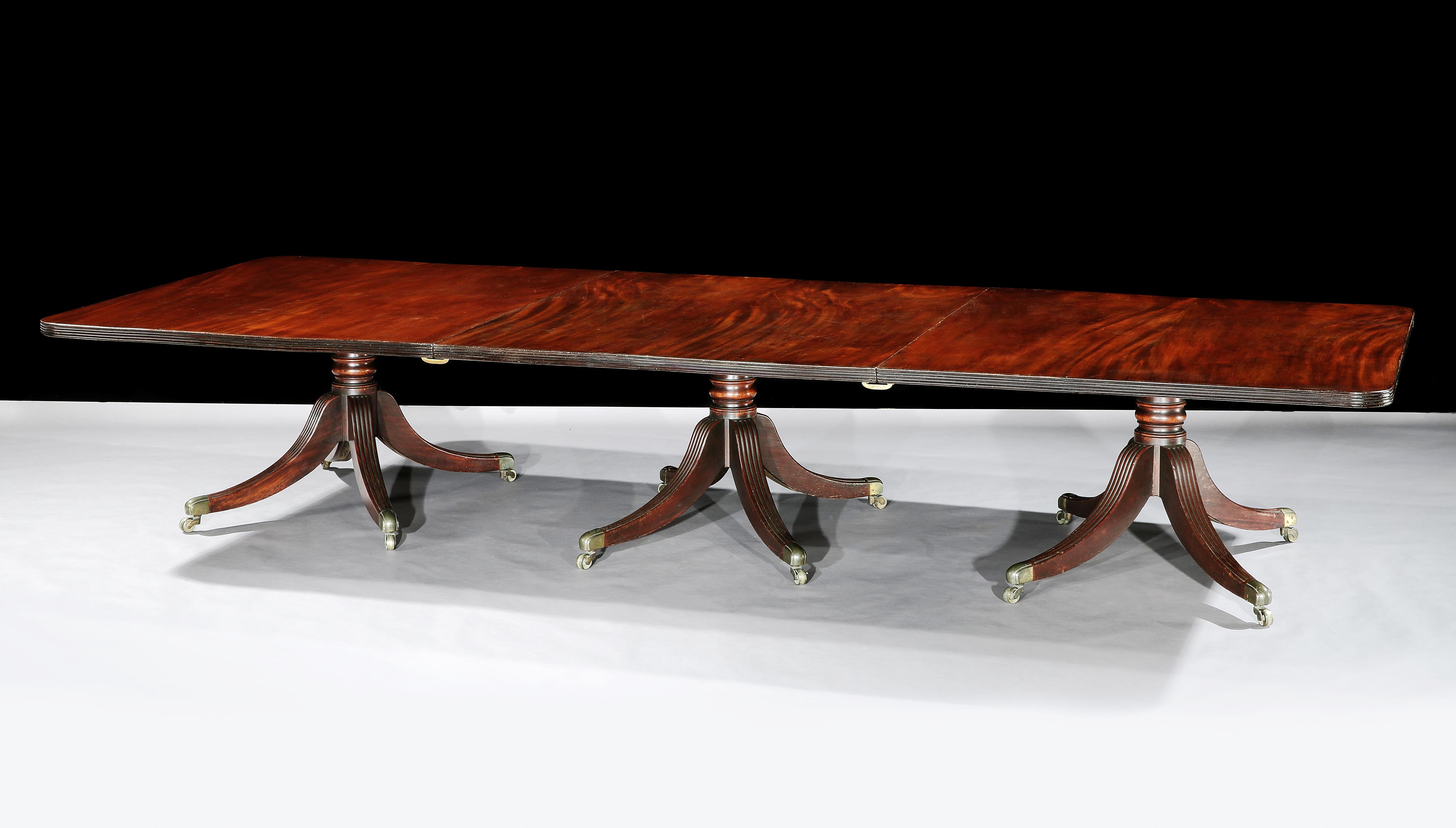 A good Irish George IV mahogany three pillar dining table. The three rectangular tops with reeded edges and two original leaves above three four splay pods with turned central columns and reeded sabre supports with brass castors. In the manner of
