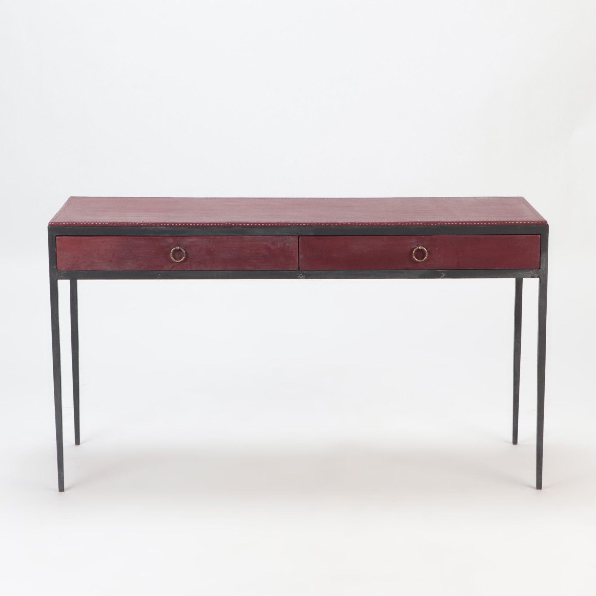 An iron and burgundy leather writing desk in the manner of Jean-Michel Frank. Contemporary. Two drawers with brass handles.