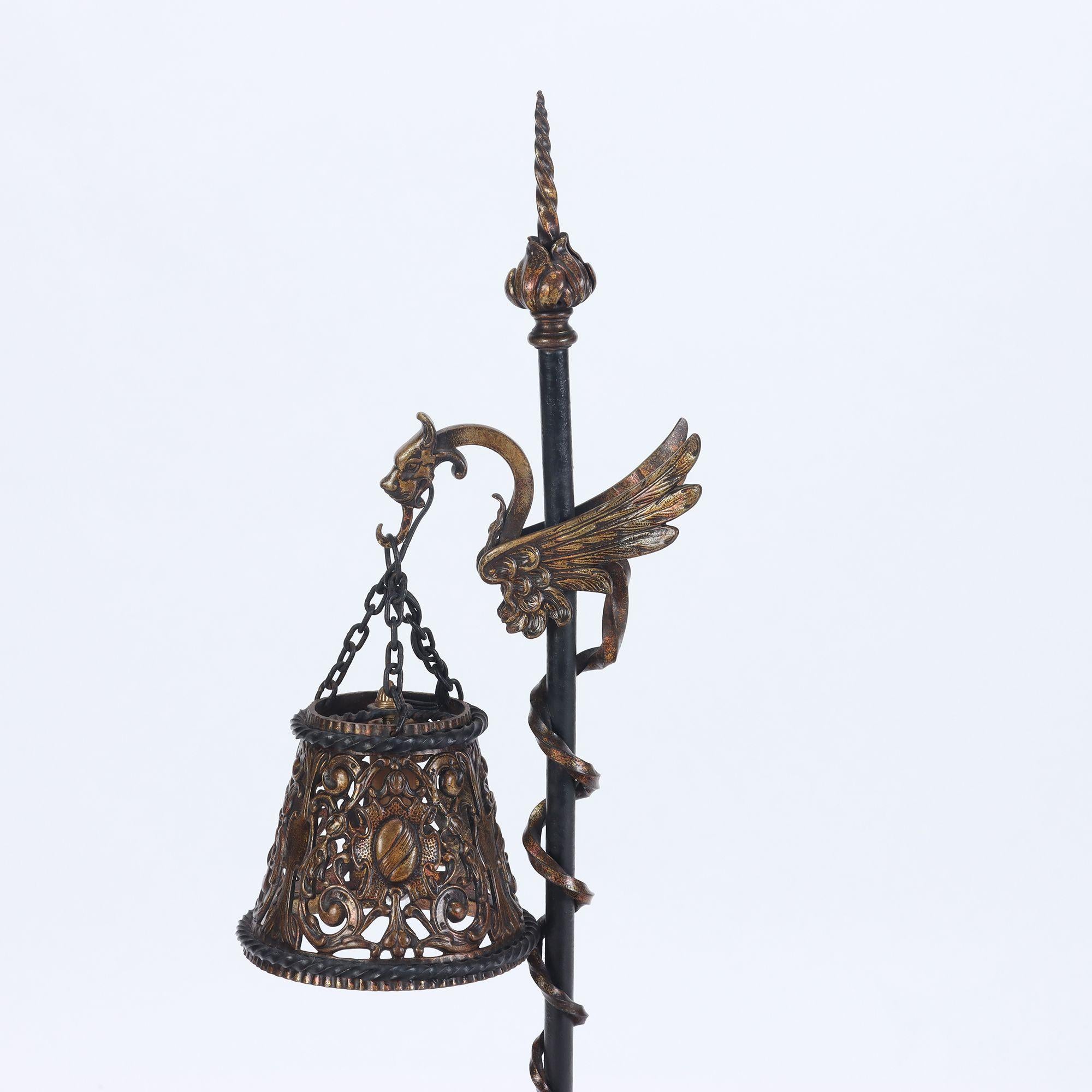 An iron and gilt decorated floor lamp with winged griffin decoration C 1900. The dragon's tail wrapping the light's standard.