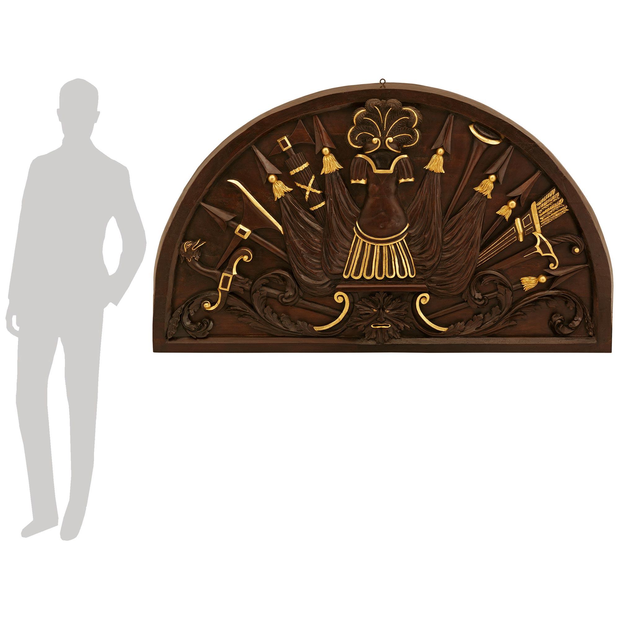 A most unique and richly carved Italian 18th century Neo-Classical st. patinated Wood and Giltwood plaque. This wonderful demi lune shaped plaque/trophy is centered at the bottom by a most charming Green Man mask with Giltwood accents and framed by