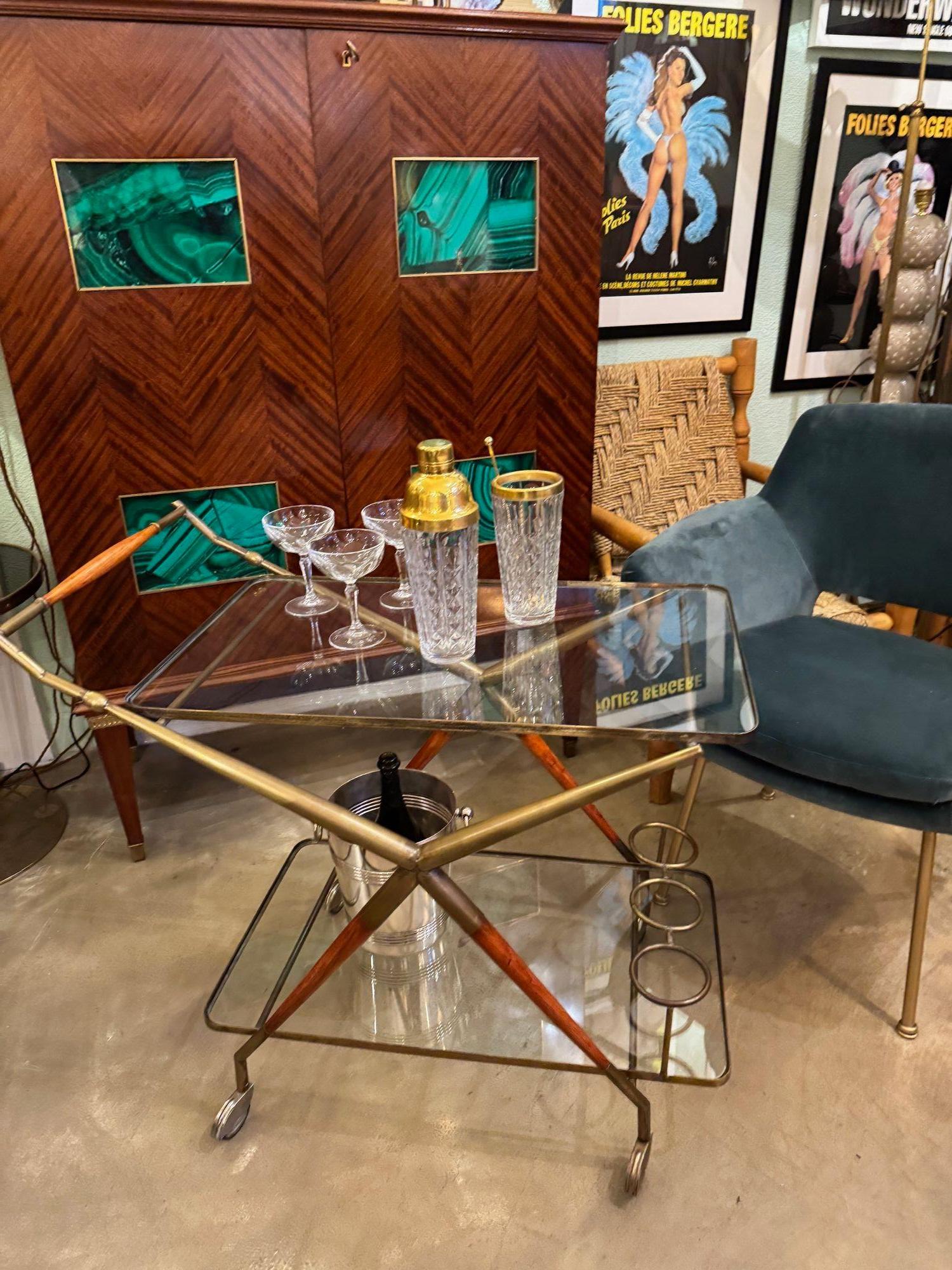 An Italian 1950s brass and lacquered wood bar trolley by Cesare Lacca with unusual top brass structure, (Usually wood) two glass shelves and brass bottle holder and original working brass castors