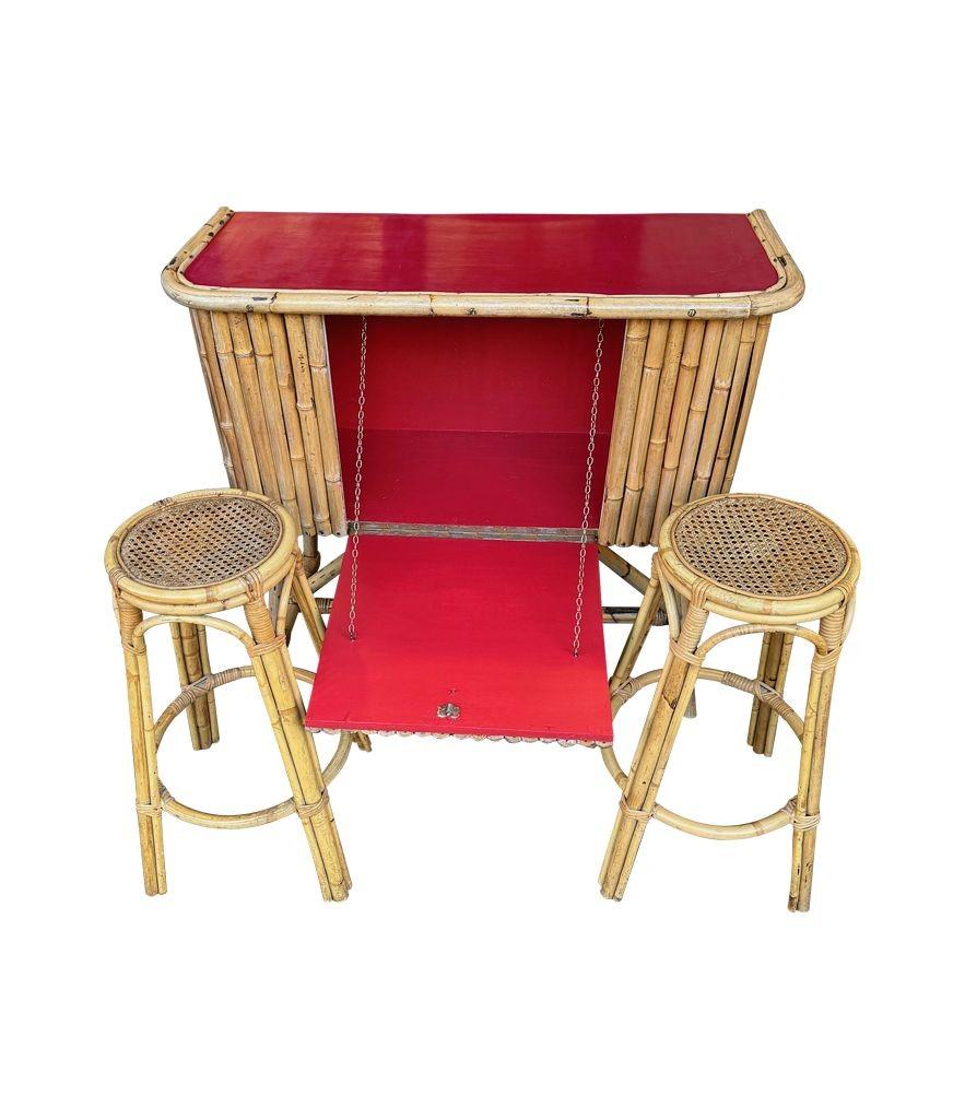 An Italian 1960s bamboo bar cabinet with orignal red laminate top and central drop down door / table. The interior finished in vibrant red as is the laminate top. With two circular bamboo stools with woven rattan seats.