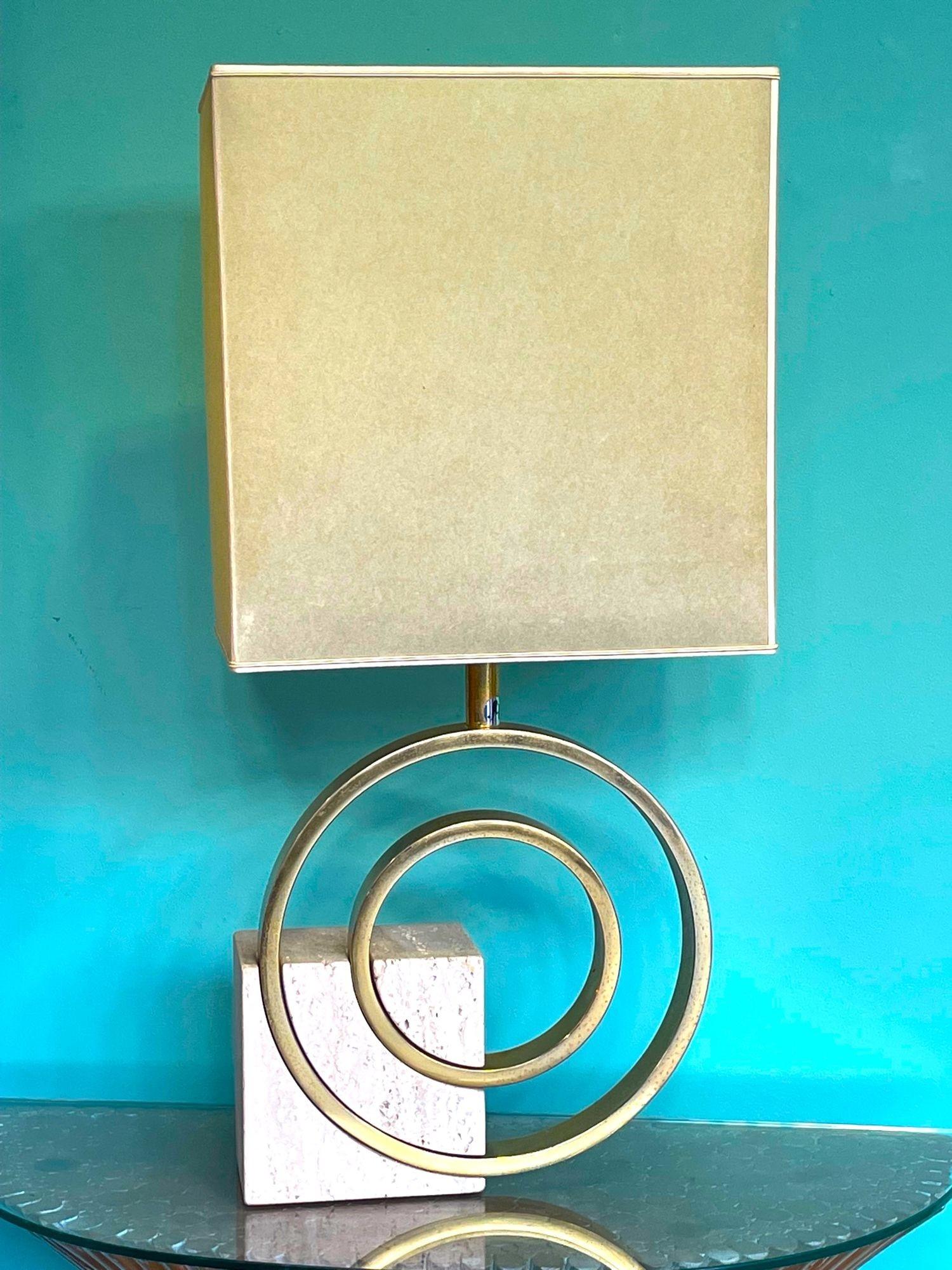 An Italian 1970s sculptural lamp by Giovanni Banci for Banci Firenze, with a solid block of travertine with brass circular rings cut into it, the larger with a single brass fitting attached, with orignal parchment shade and 