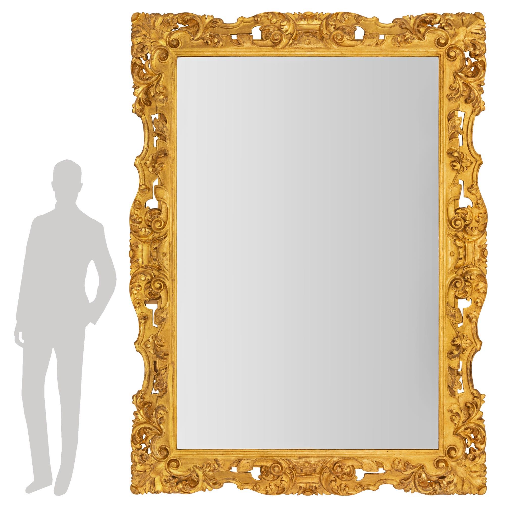 Un étonnant et très impressionnant miroir baroque italien du 19ème siècle en bois doré. Le miroir conserve sa plaque d'origine encadrée d'une fine bordure mouchetée. Le cadre présente un ensemble exceptionnel de beaux mouvements à volutes percées