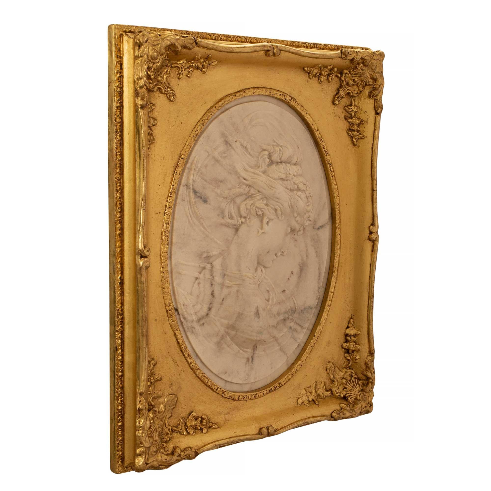 A stunning Italian 19th century white Carrara marble finely carved oval relief in a beautiful giltwood frame. The wonderfully executed white Carrara marble relief is of an ethereal classical maiden with her hair in a period updo. The marble relief