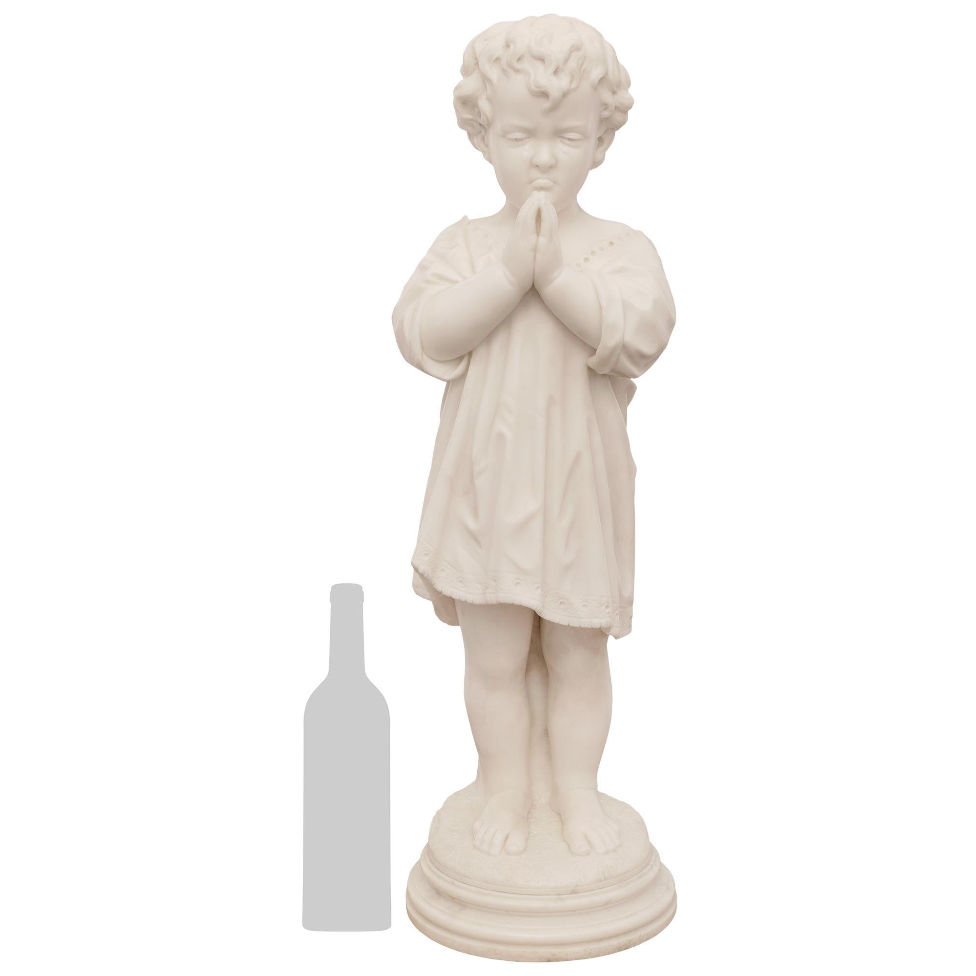 A charming Italian 19th century white Carrara marble statue of a young boy signed Pietro Franchi, Rome. The praying boy is raised on a circular mottled pedestal and is wearing classical attire while holding his hands together to pray. A tear is