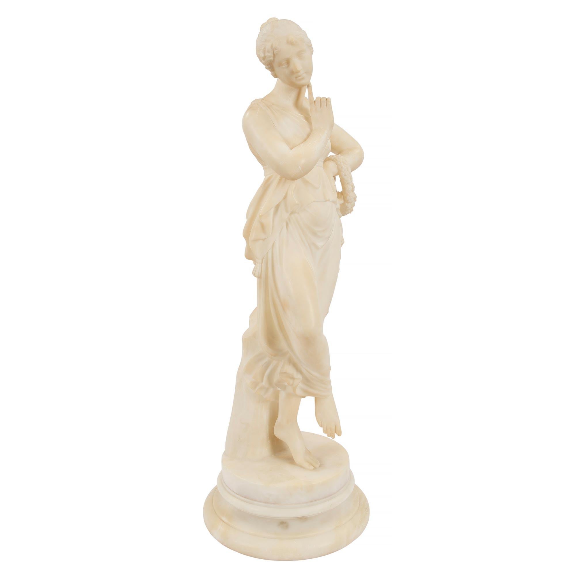 A most elegant Italian 19th century neoclassical style alabaster statue of a maiden. The statue is raised by a circular mottled base where the beautiful maiden stands. She is dressed in wonderfully sculpted period attire with one hand on her hip