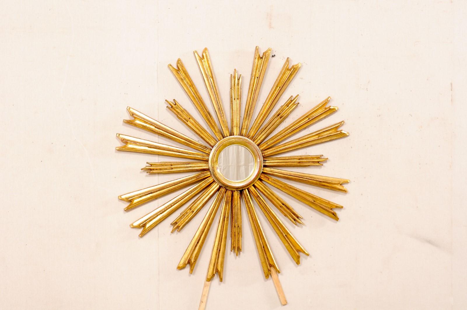 An Italian carved and gilded wood sunburst with mirror. This vintage wall ornament from Italy features a small round-shaped mirror at center within a molded gold and silver gilt wood frame, surrounded by a serious of carved and gold gilt rays