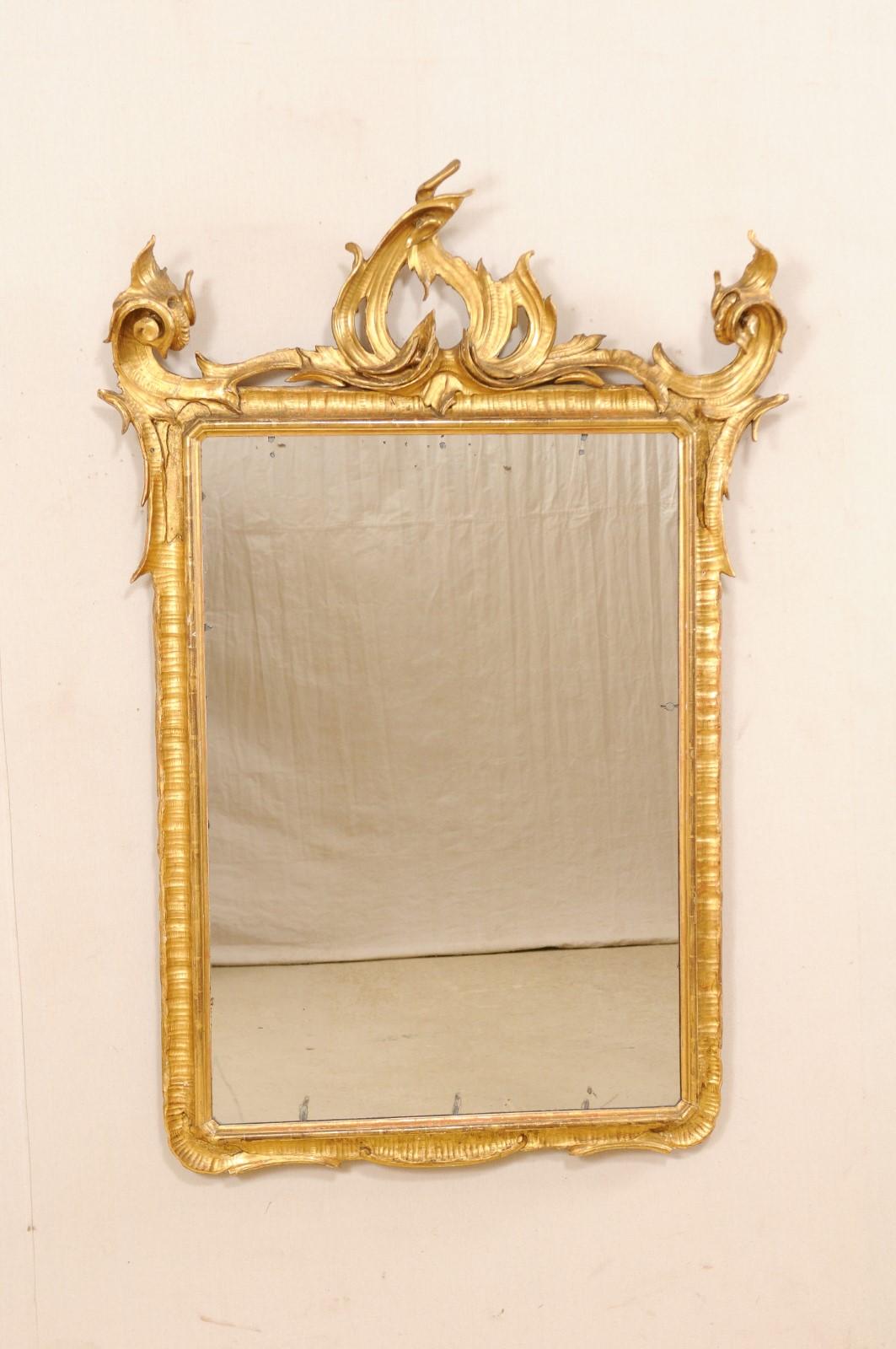 An Italian carved and giltwood mirror from the early 20th century. This antique mirror from Italy is fabulous modern interpretation of Baroque design. It has an overall rectangular-shape with a richly carved crest in Baroque style with a more