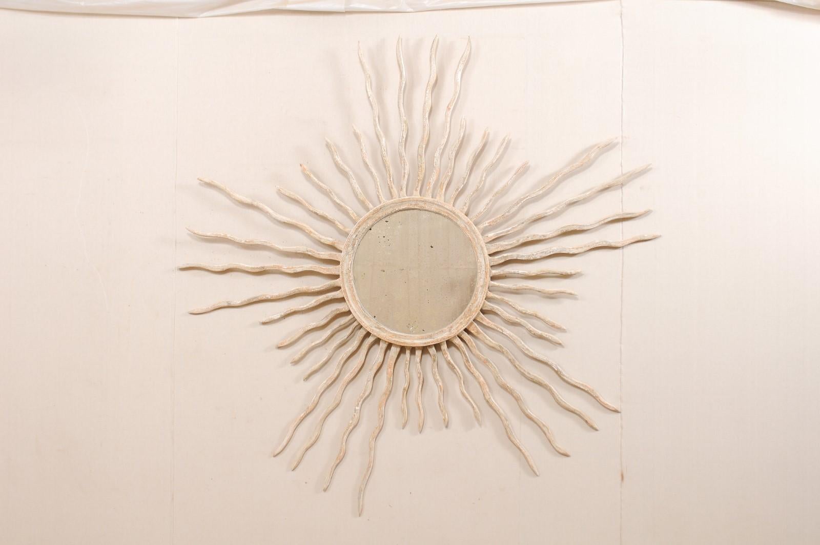 A large sized Italian round mirror with sunburst surround. This custom mirror from Italy, designed by an artisan crafter, features a round-shaped and antiqued center glass, with is set within a wood surround which bursts with rays extending outward