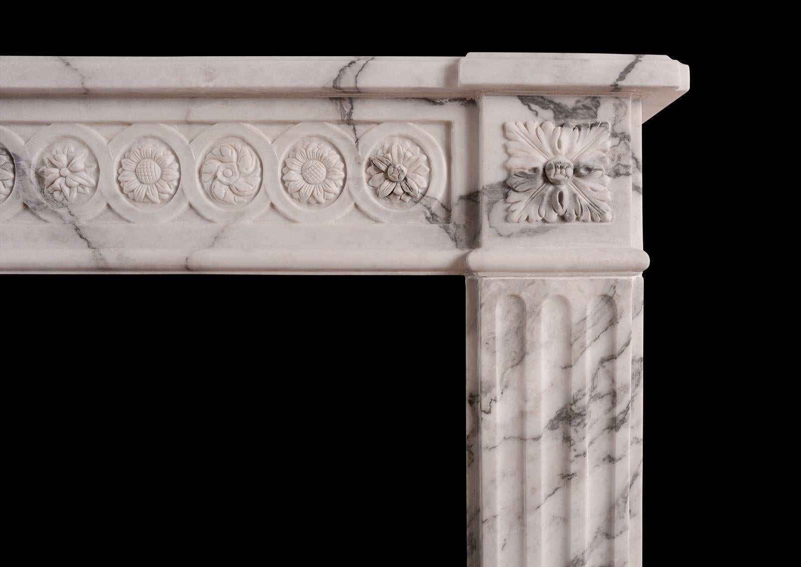 A good quality French Louis XVI style Italian Arabescato marble fireplace. The finely carved guilloche frieze with rosettes, acorns and foliage throughout, flanked by carved square paterae. The jambs with stop flutes with carved husks. Breakfronted