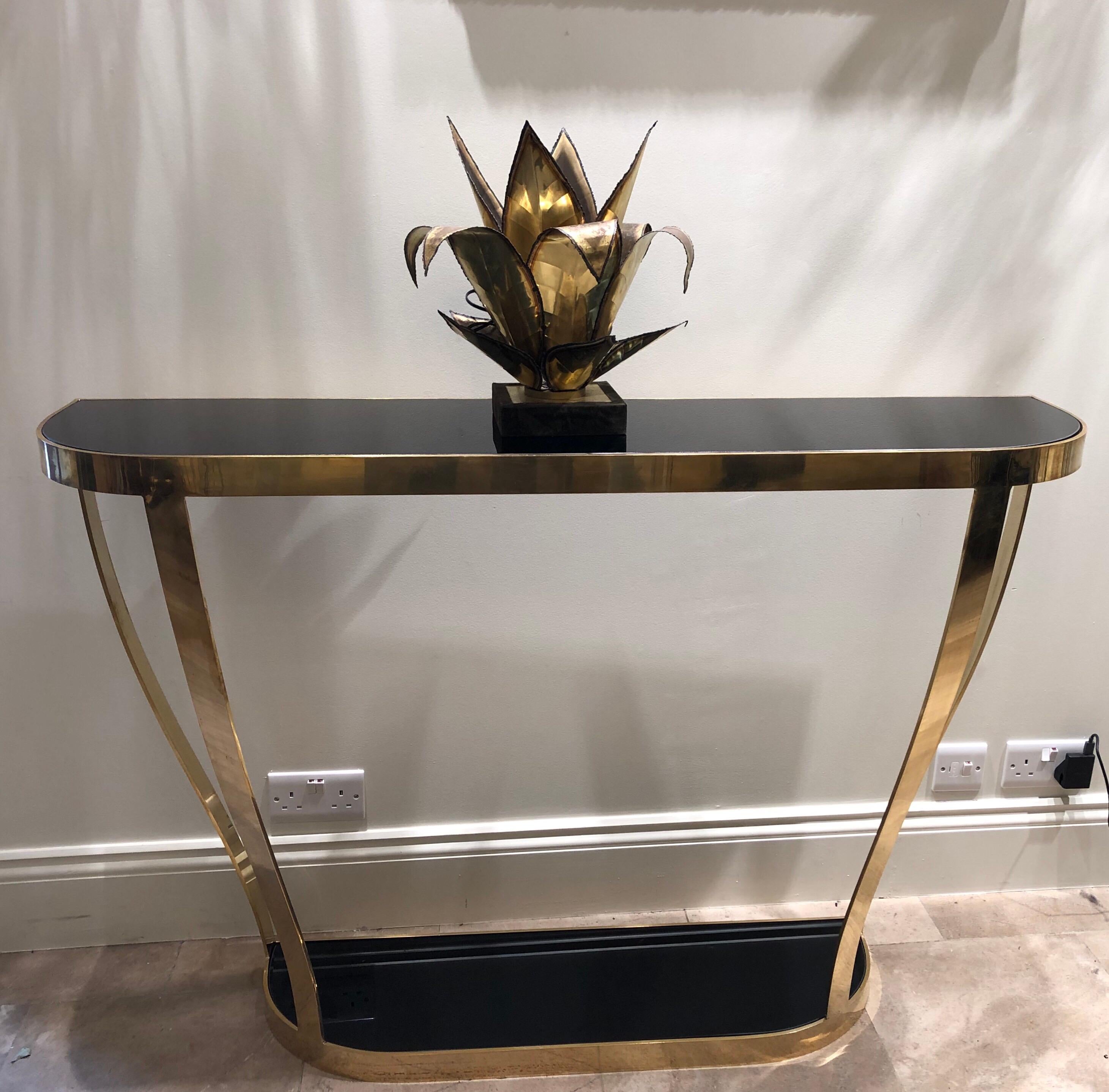 A console table by Rkade Studio which has been crafted in curved brass and black glass. There are a pair available or they can be sold separately. There is a bottom black glass shelf.