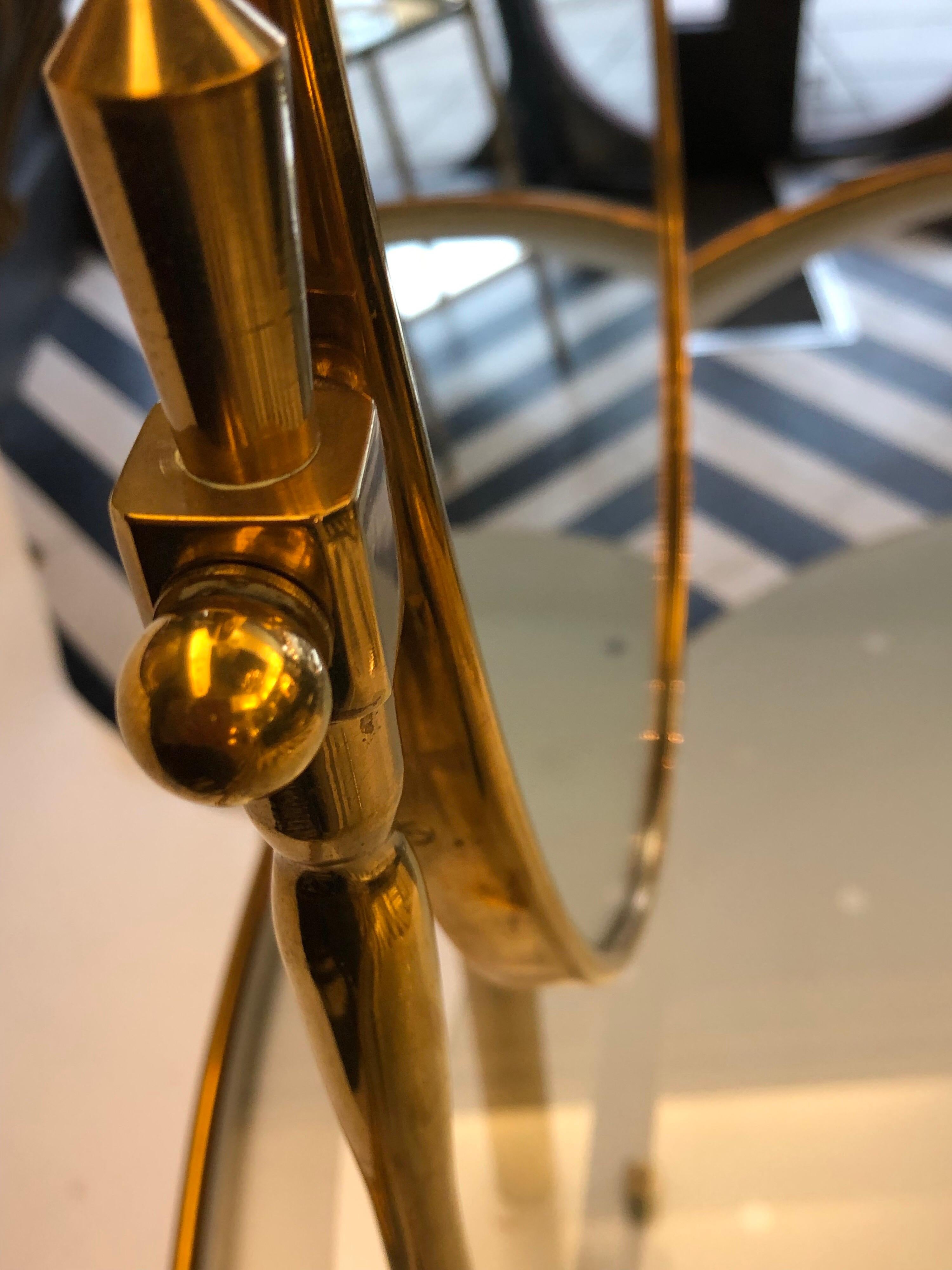 A very elegant two tiered kidney shaped dressing table made of a brass frame and glass shelves. The lower shelf is opaque with a polka dot design and the top is clear. The adjustable mirror is fixed on top and the whole table is lit from beneath.