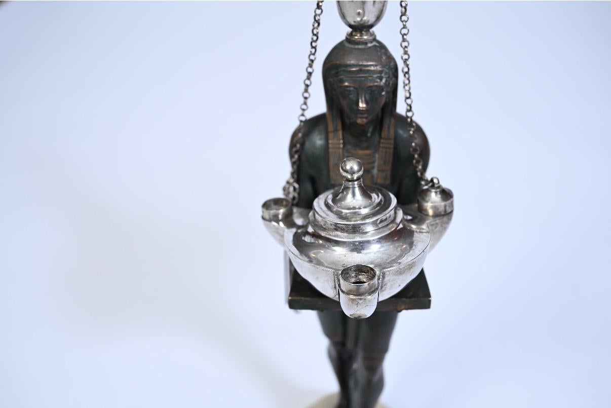 Una rara e teatrale lampada a olio italiana in bronzo e argento, realizzata a Roma intorno al 1800, questo pezzo eccezionale è ben lontano da un tipico oggetto utilitario: è un tour de force scultoreo infuso di esotismo, ingegnosità tecnica e