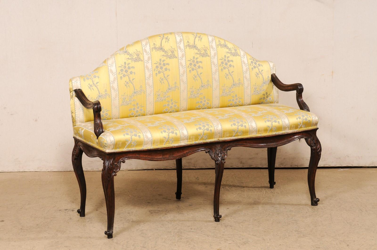 An Italian upholstered and carved-wood settee, turn of the 18th and 19th century. This sweet antique love seat from Italy features a low-profile arched back with squared shoulders, from which the nicely carved-wood arms emerge and slope down into