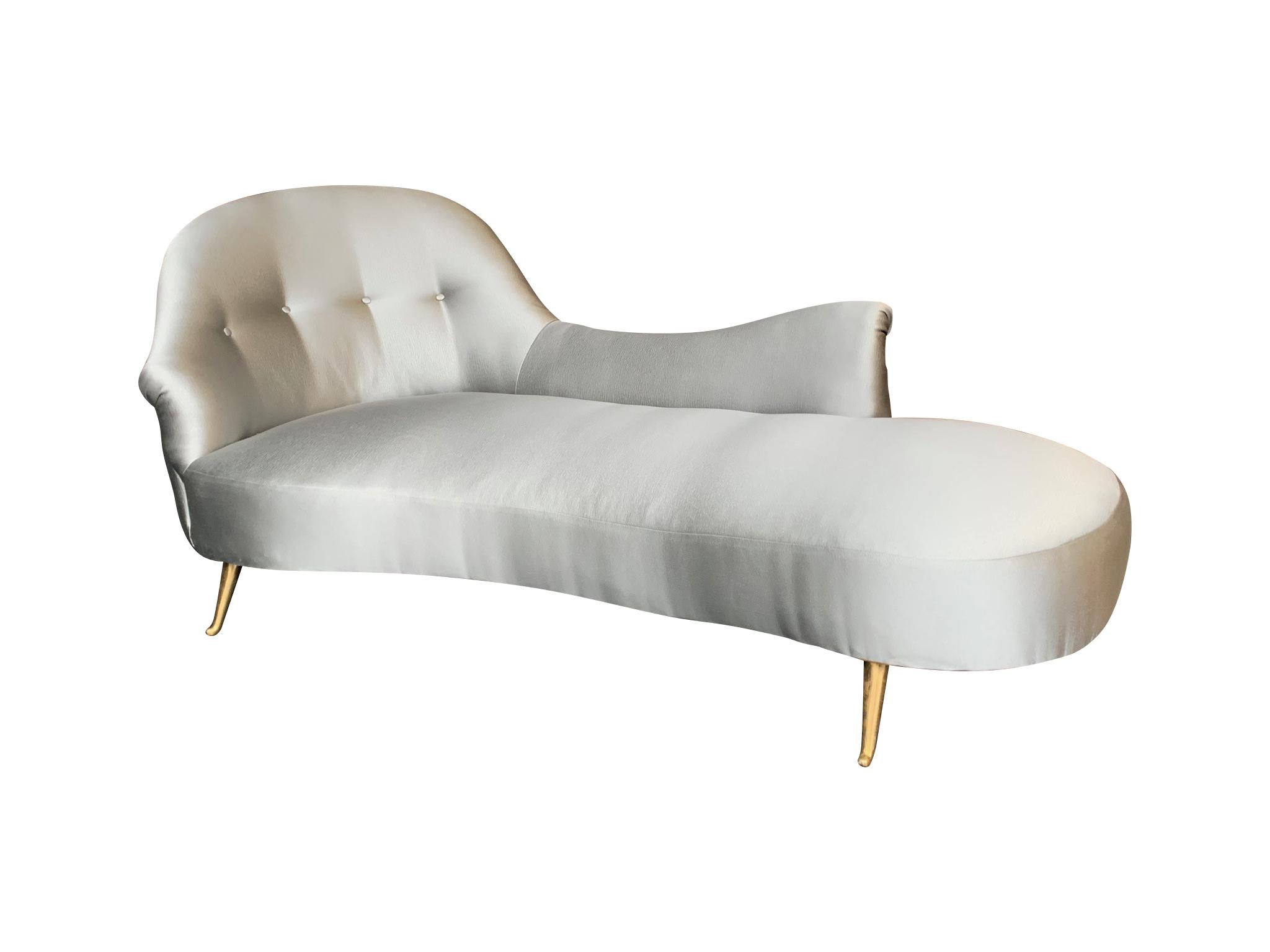 An Italian curved chaise loungere-upholstered in champagne grey fabric with button back and brass curved feet.