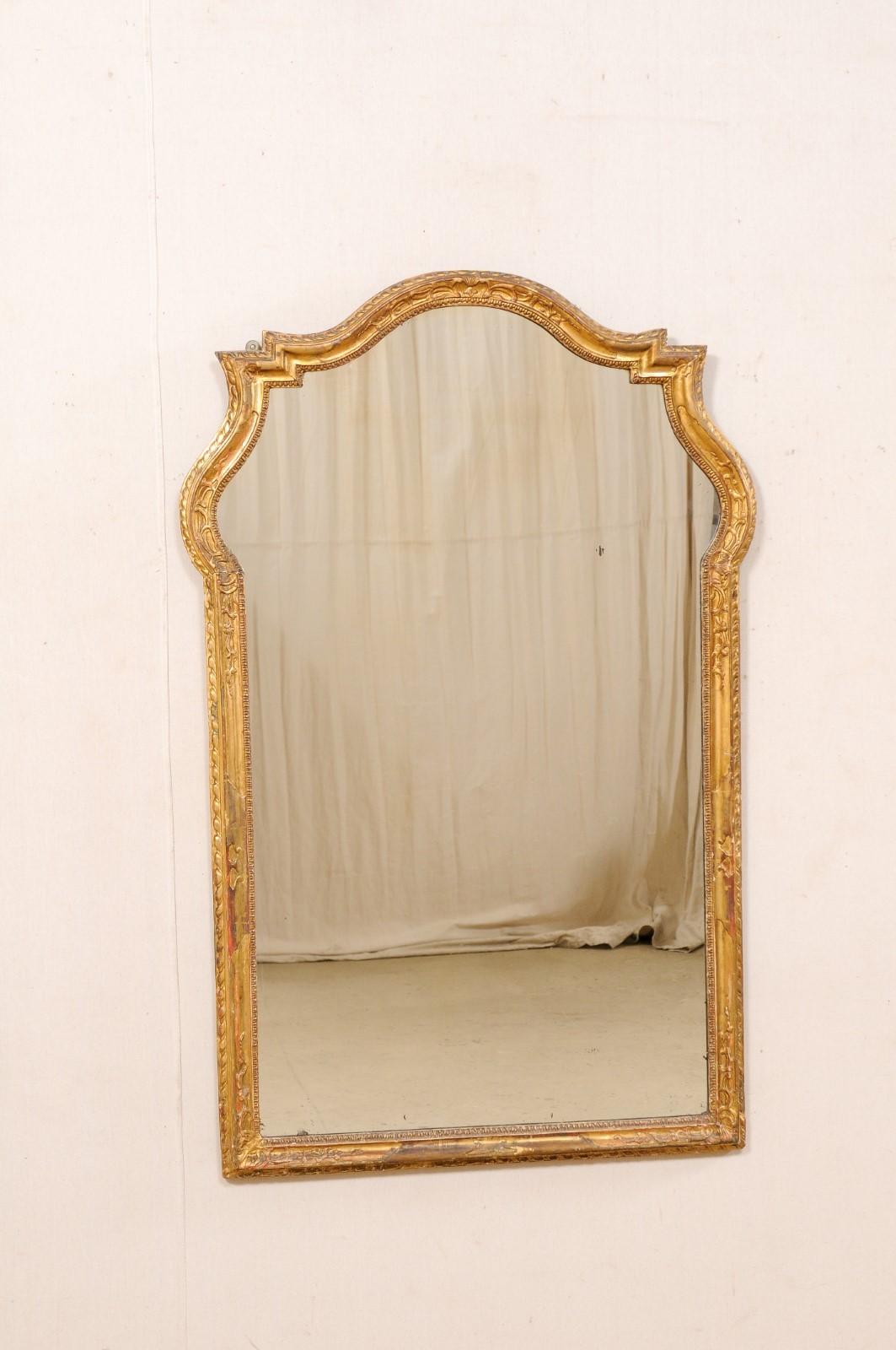 An Italian carved-wood mirror, with its original finish, from the early 19th century. This antique mirror from Italy has a hand-carved and beautifully textured surround with varied trim moldings, shapely top lines include a gracefully arched crest,