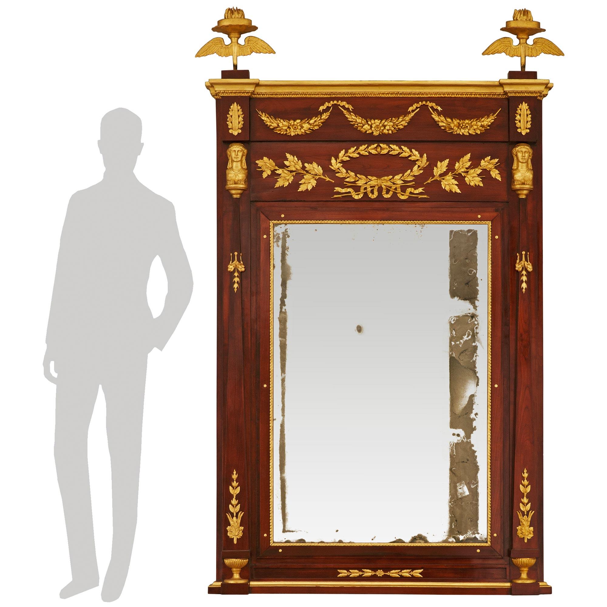 Un'imponente specchiera in mogano patinato e legno d'orato dell'inizio del XIX secolo. Questo splendido specchio in mogano è decorato con un filo di alloro in legno dorato nella parte inferiore, che conduce alle coppe a sinistra e a destra. Ciascuna