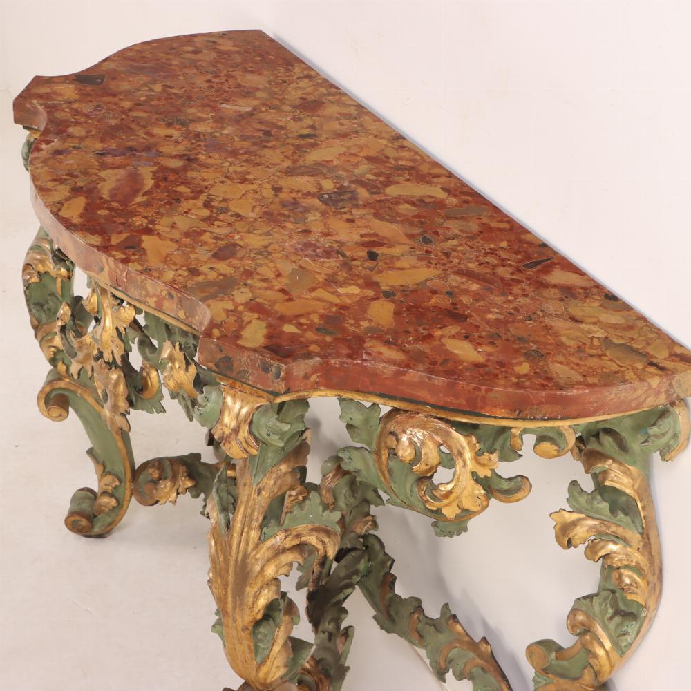 The green painted and gilt carved frame boasts a faux marble decorated top above a ornately carved frame with overall rococo and foliate motifs to the apron and the four shapely cabriole legs joined by an X-shaped stretcher and terminating in