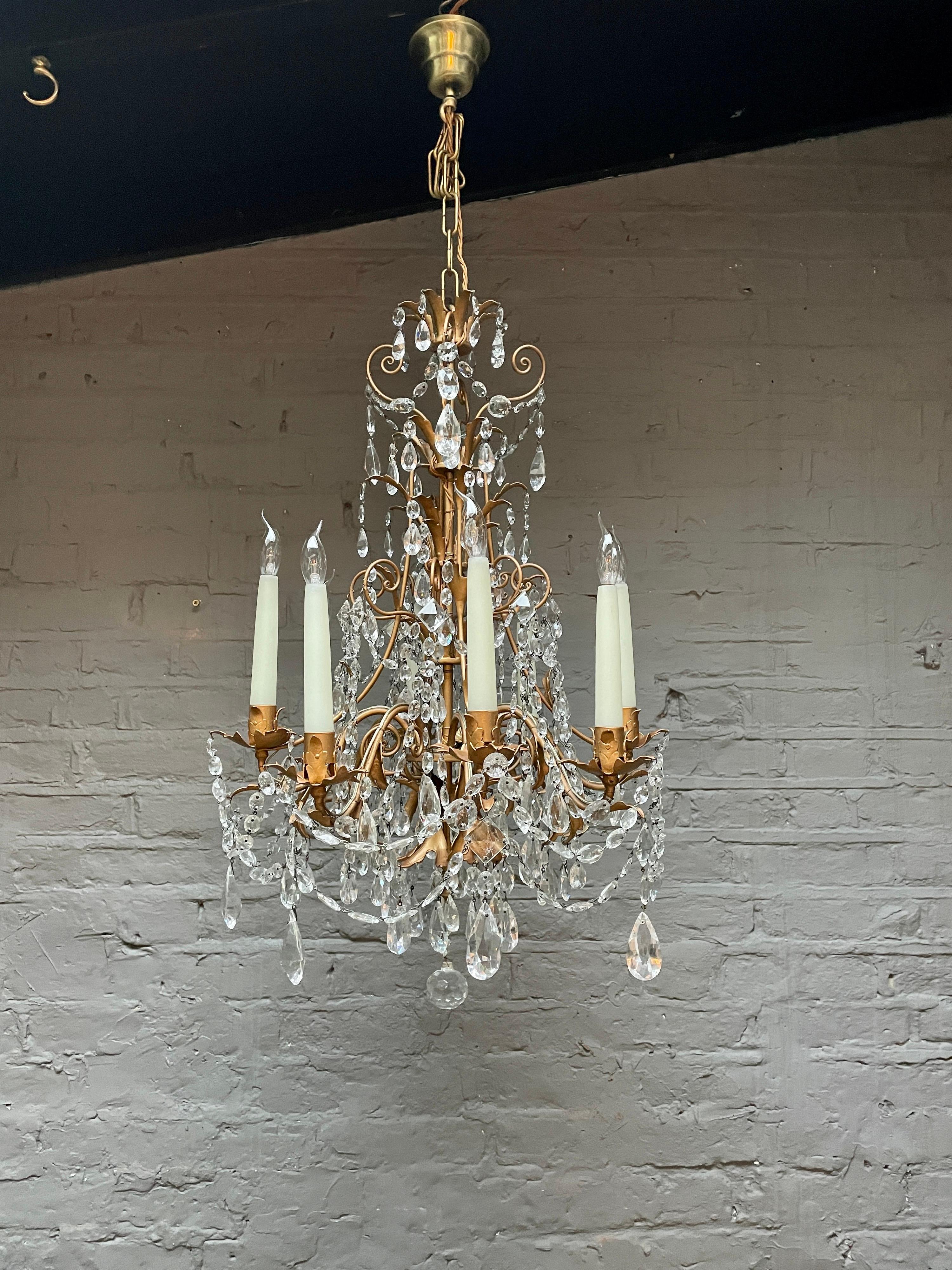 A decorative gilt tole and crystal chandelier from the mid 20th century, probably Italian rather than French, with eight arms having long slim and tapering candle holders which are supported on alternately raised arms, dressed in crystal with around