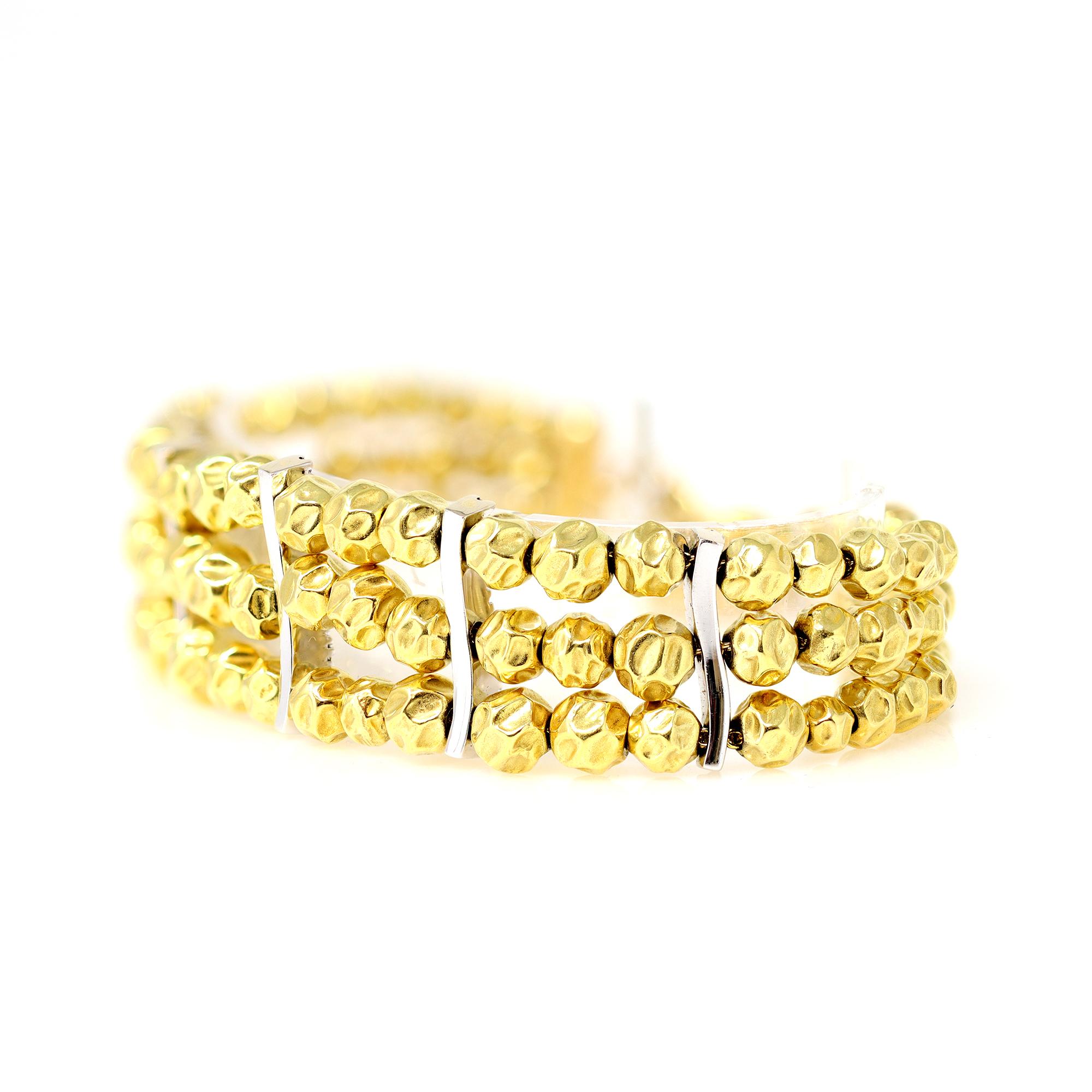 A modern gold beads bracelet circa 1990 featuring 3 lines of graduated hammered yellow gold beads, accented with diamond spacers and ending at the clasp with a small diamond ball charm. The bracelet is executed in 18 karat yellow and white gold and
