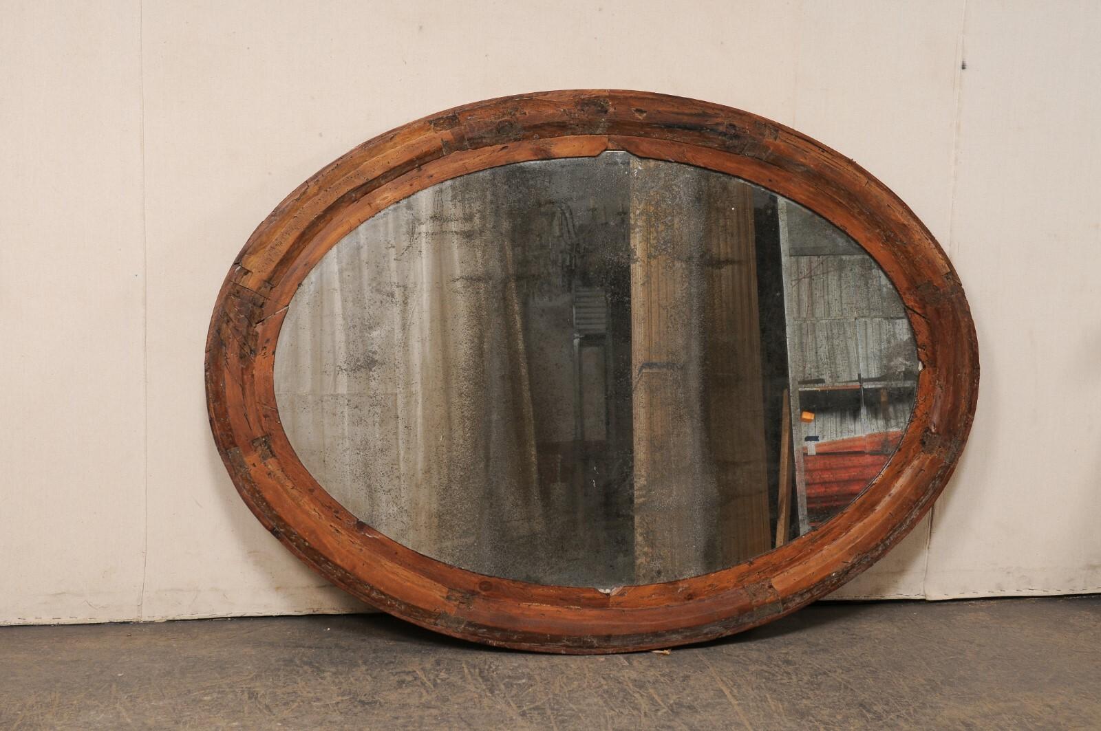 An Italian large-sized oval mirror, in a beautifully rustic wooden frame, from the early 20th century. This antique mirror from Italy has an oval shaped center glass, surrounded within an oval-shaped wooden frame. Though the design is simplistic,