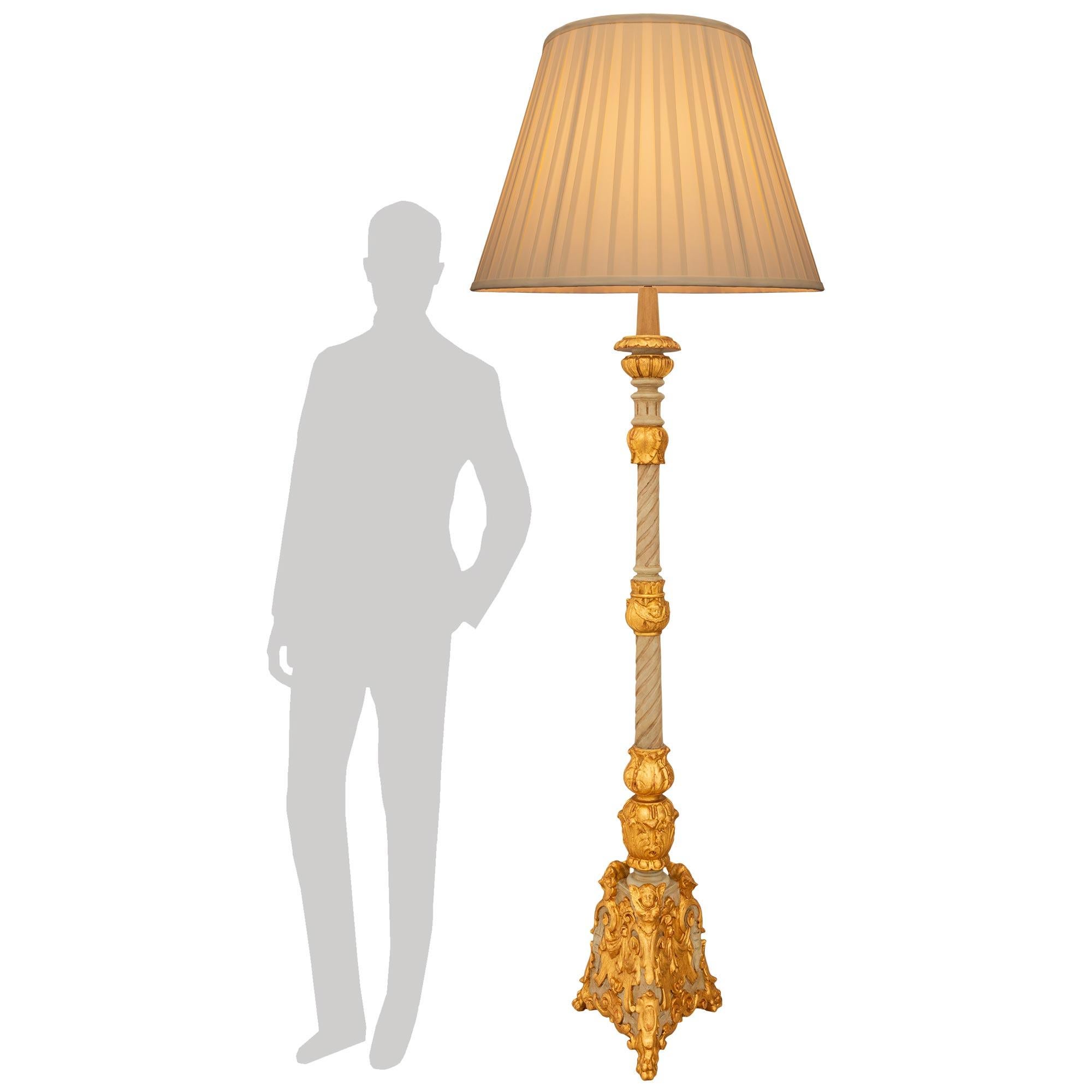 Eine attraktive und elegante italienische Barocklampe aus dem späten 18. Jahrhundert, patiniert und aus Giltwood. Diese beeindruckende Stehlampe steht auf einem dreieckigen Sockel auf Pfotenfüßen und ist mit Giltwood-Rollwerk und geflügelten Putten