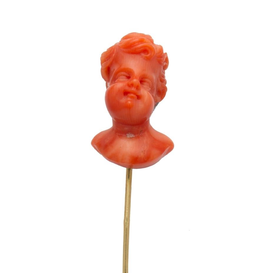 An Italian late 19th century coral stick pin, featuring the bust of cherub realistically carved out of coral, to an 18ct yellow gold pin fitting, circa 1870, the bust measuring approximately 2.5 x 1.5cm, the pin measuring approximately  7.3 cm long,