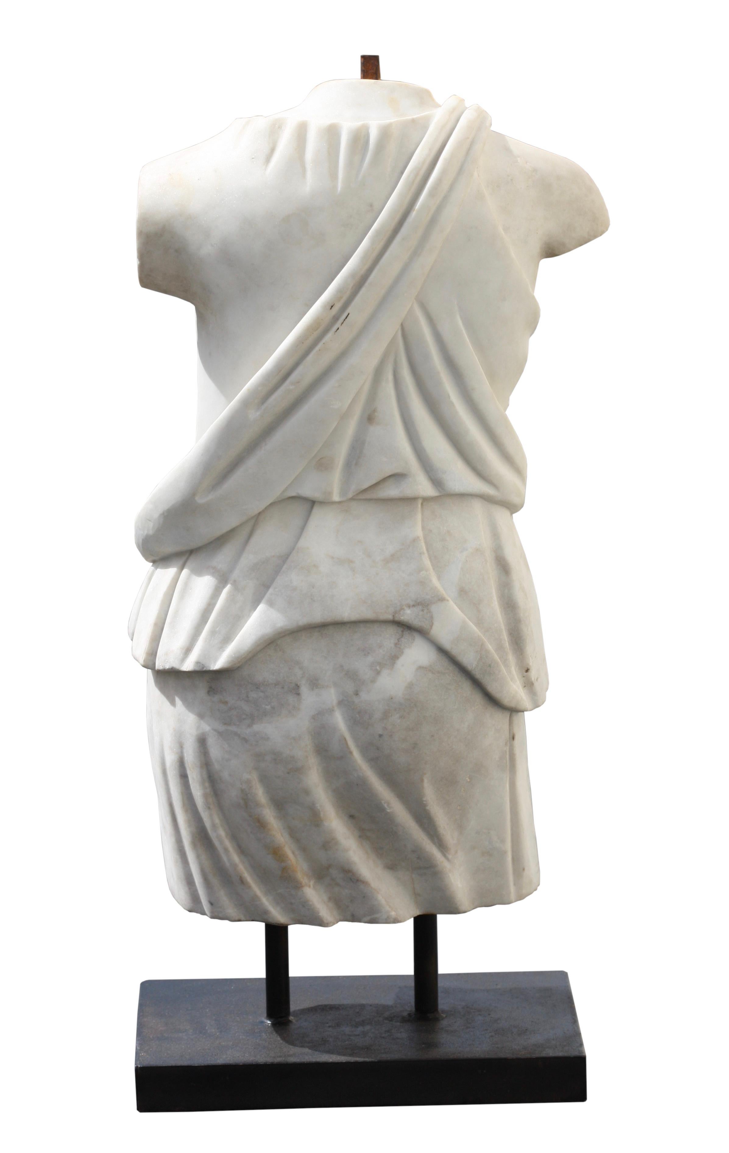 An Italian marble figure of a torso, 19th/20th century
wearing a tunic falling from her right shoulder and leaving the breast bare, both ends of the fillet falling over the nape of her neck, on a bronze base, height 81 cm., 32 in.