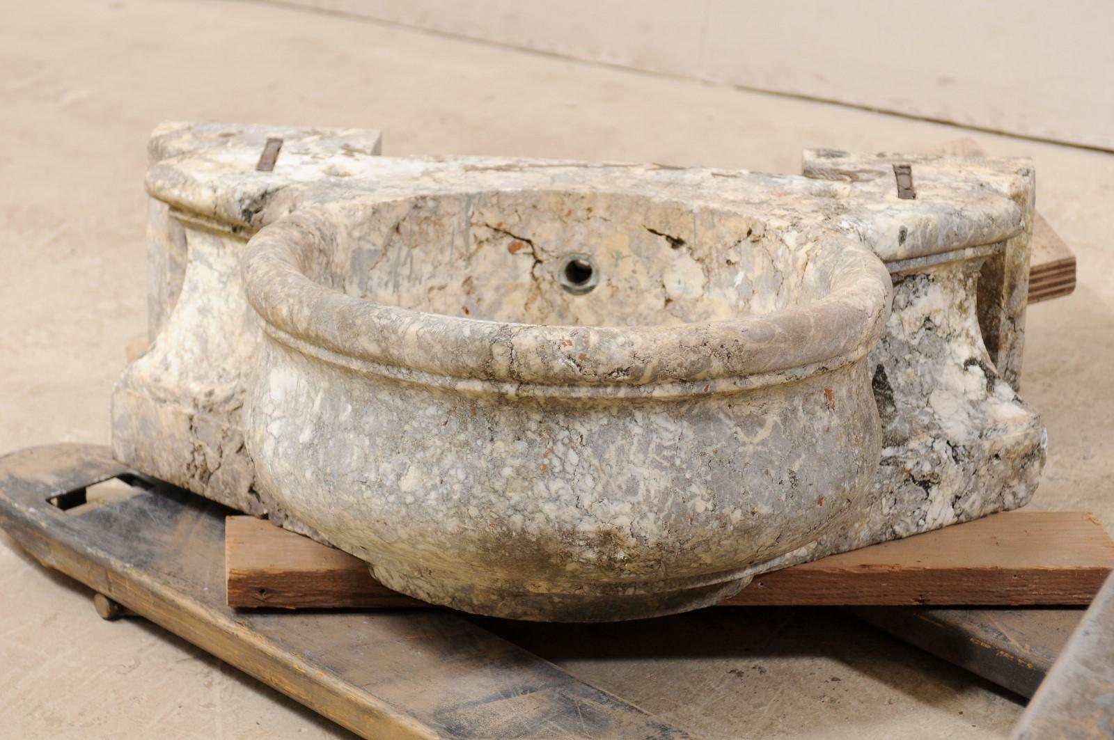 An elegant Italian marble basin from the 19th century. This antique fountain base from Italy features a rounded center basin, with bulbous shape and thick, rounded lip, which is flanked with a pair of decoratively carved and canted side pieces. The