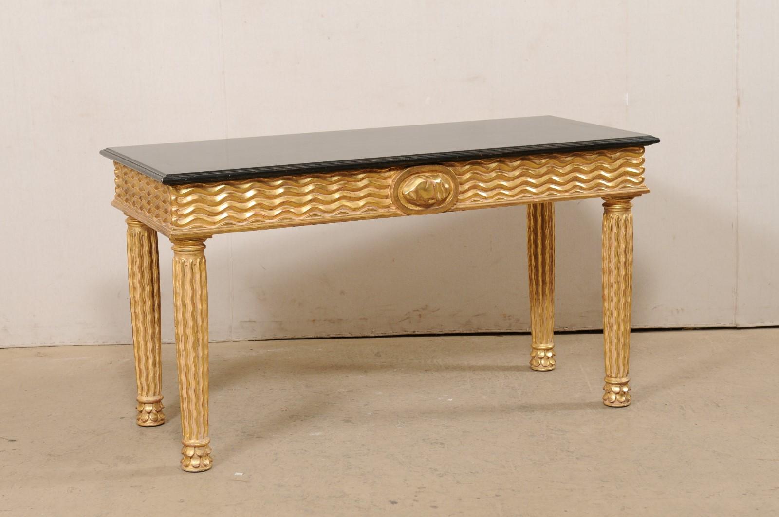 An Italian hand-carved and gold leaf console table, circa 1980's. This vintage table from Italy has been masterfully hand-carved in a fabulous wavy motif about the skirt and legs. A whimsically carved oval cartouche with 