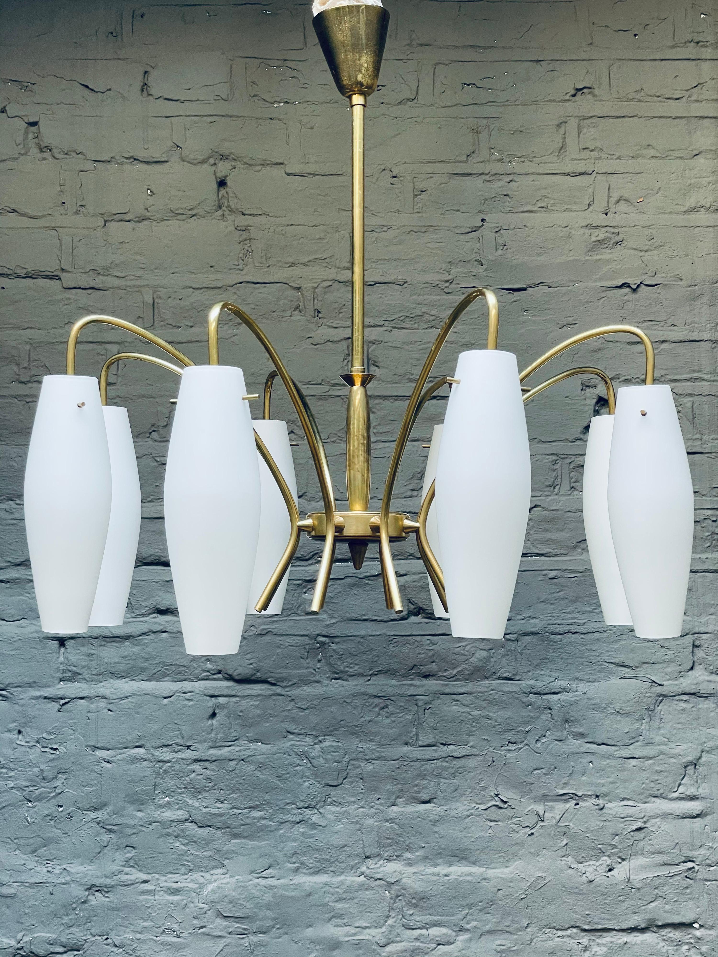 An elegant Italian midcentury brass chandelier with eight arms and cylindrical opaque shades.