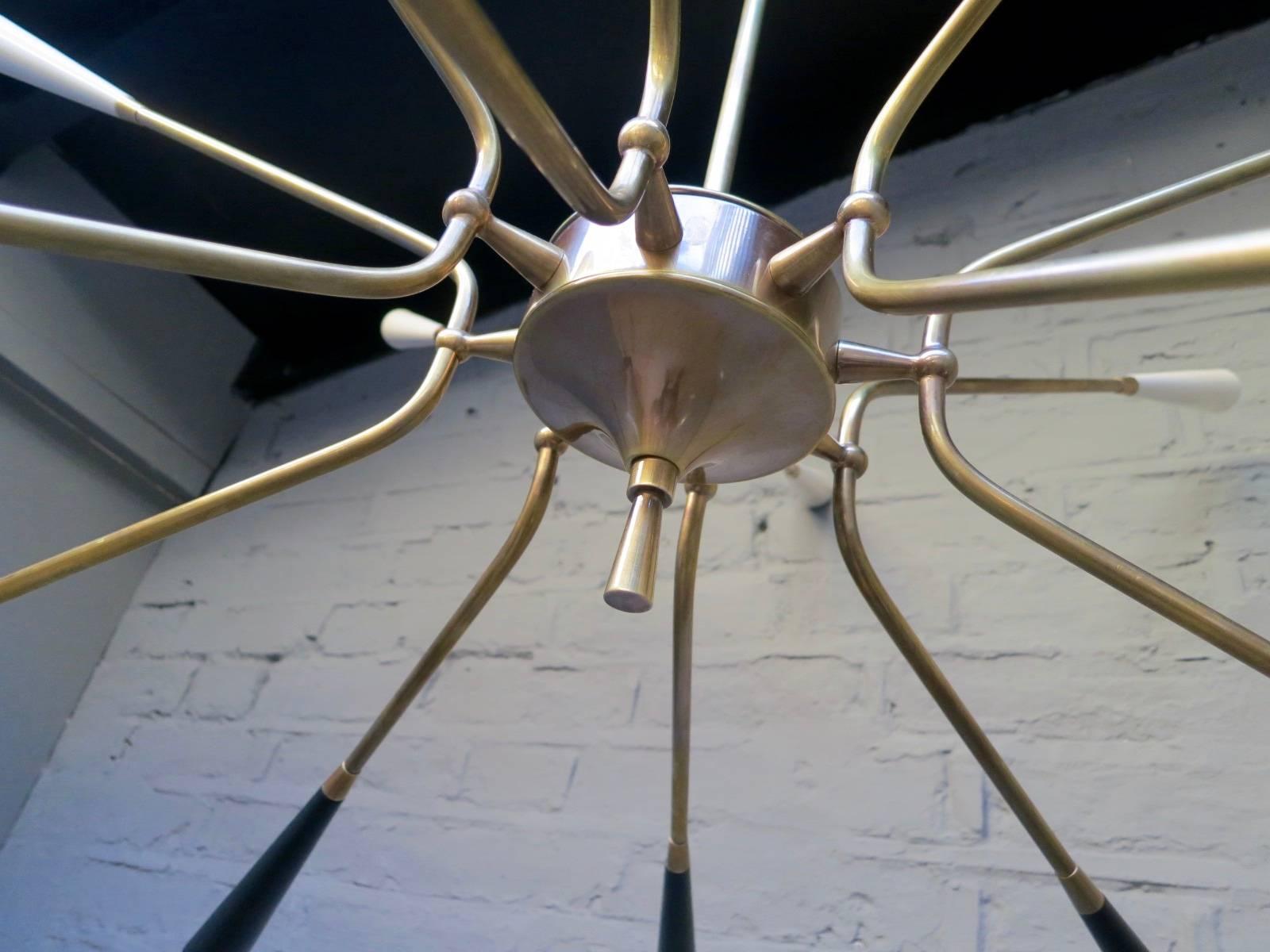 A large 16-arm Sputnik chandelier in brass with long tapered bulb holders in black and ivory, Italian Mid-Century Modern period ceiling light.