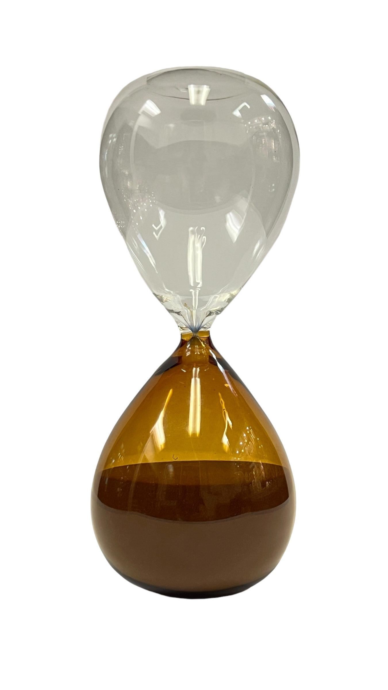 An Italian Mid-Century Modern Murano Hour Glass Sand Timer handblown in Murano Italy with a clear and amber coloration with gold colored sand. The sand flows easily through the hourglass and is unsigned. 

Measurements: 
height: 10 in. x diameter: 4