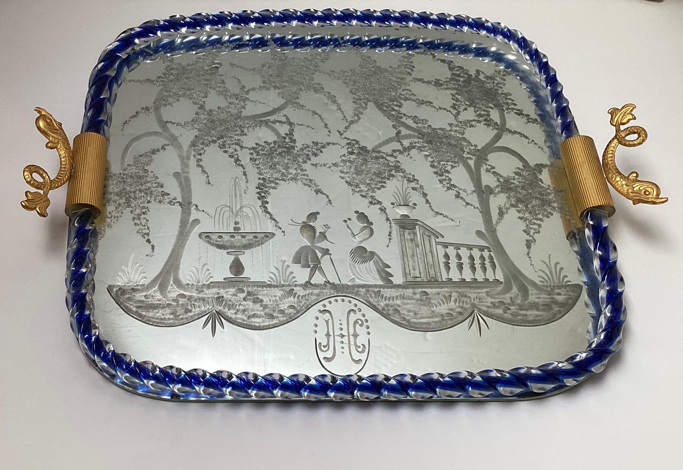An elegant Murano mirrored glass vanity tray with cobalt twisted glass gallery edge.  The etched design depicting a Venetian scene with courting couple.  The gold tone metal handles with dolphin motif, Ital, Circa 1950.  Measures 18 inches by 13